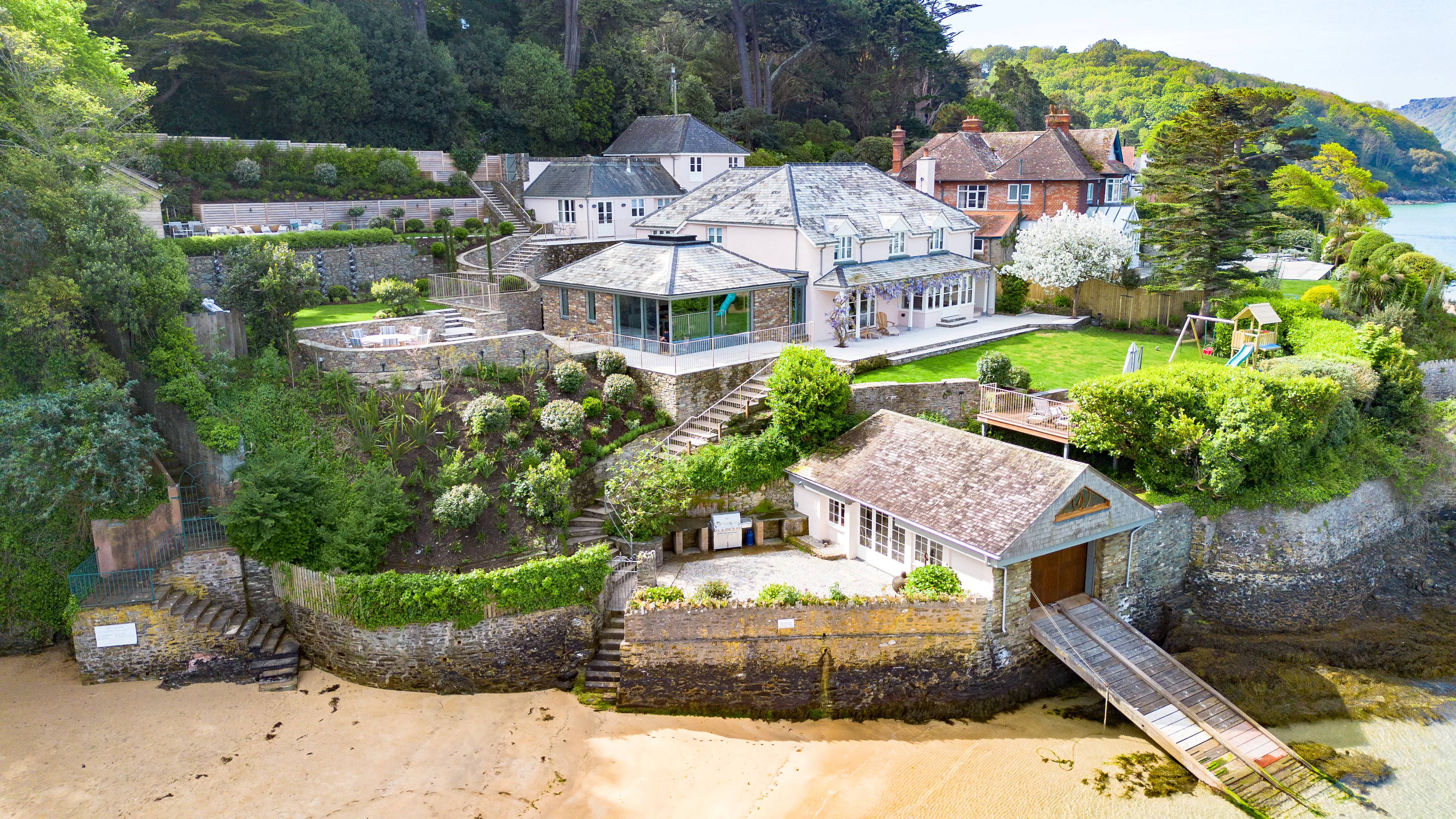 A contemporary Douglas fir glulam framed kitchen extension to a stone cottage with a terraced garden leading down to the bank of an estuary