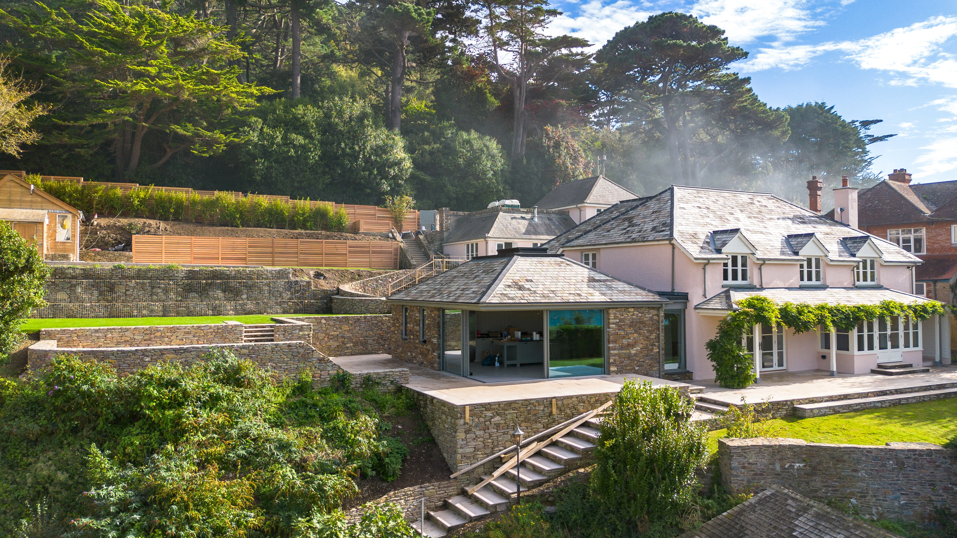 A contemporary Douglas fir glulam framed kitchen extension to a stone cottage with a terraced garden