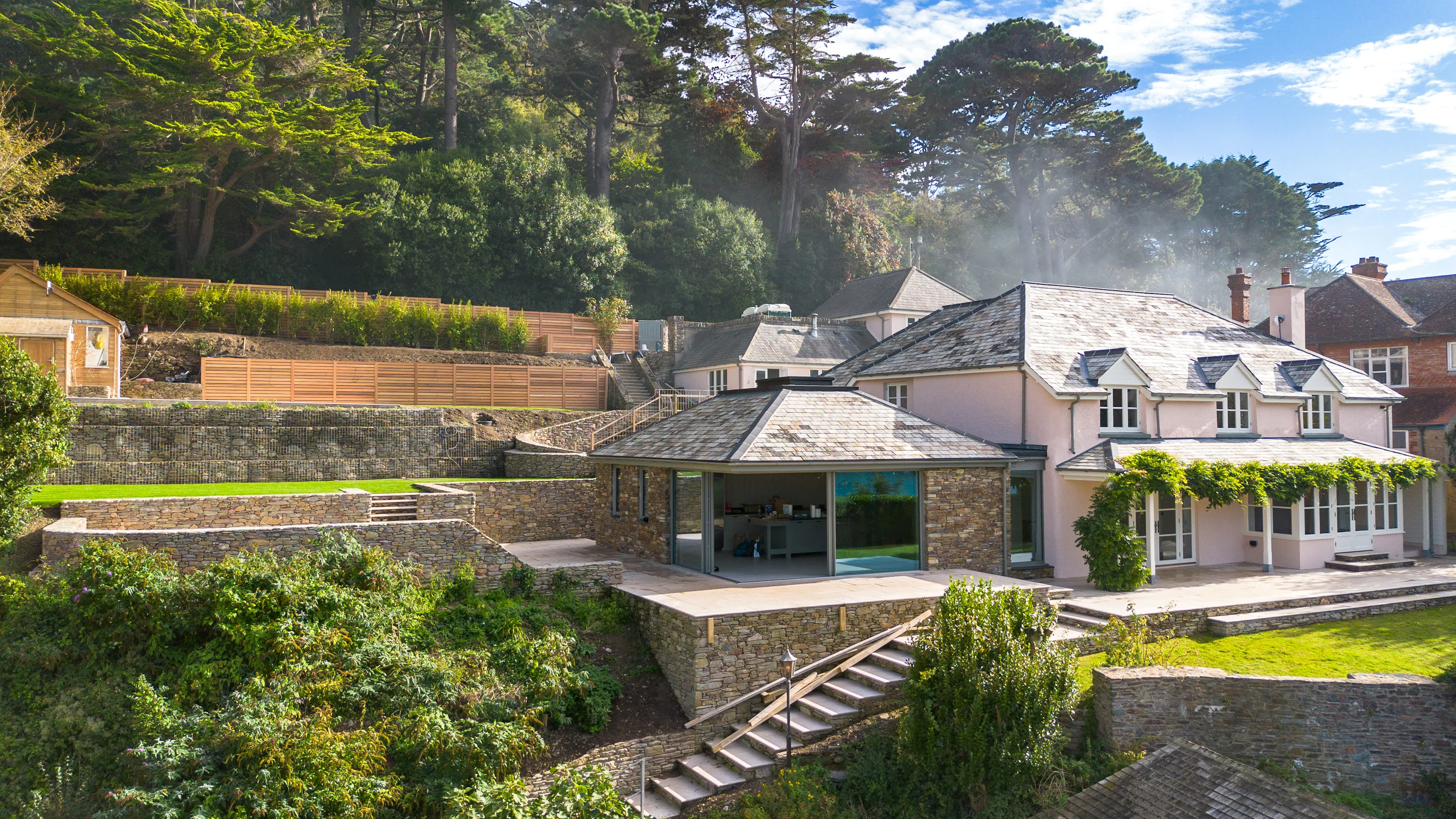 A contemporary Douglas fir glulam framed kitchen extension to a stone cottage with a terraced garden