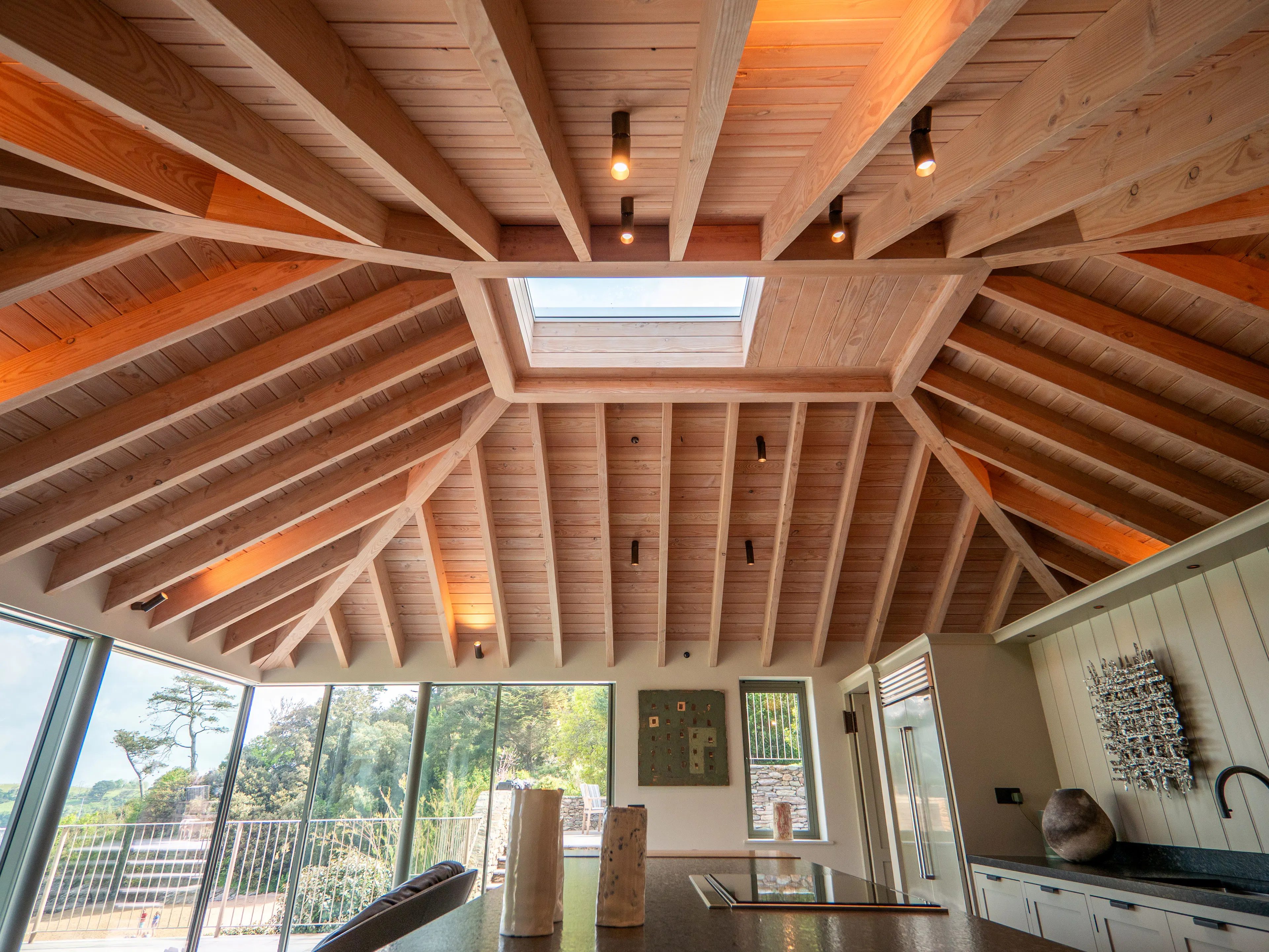 A contemporary Douglas fir glulam framed kitchen extension with a large kitchen island and modern armchairs by glazed sliding doors