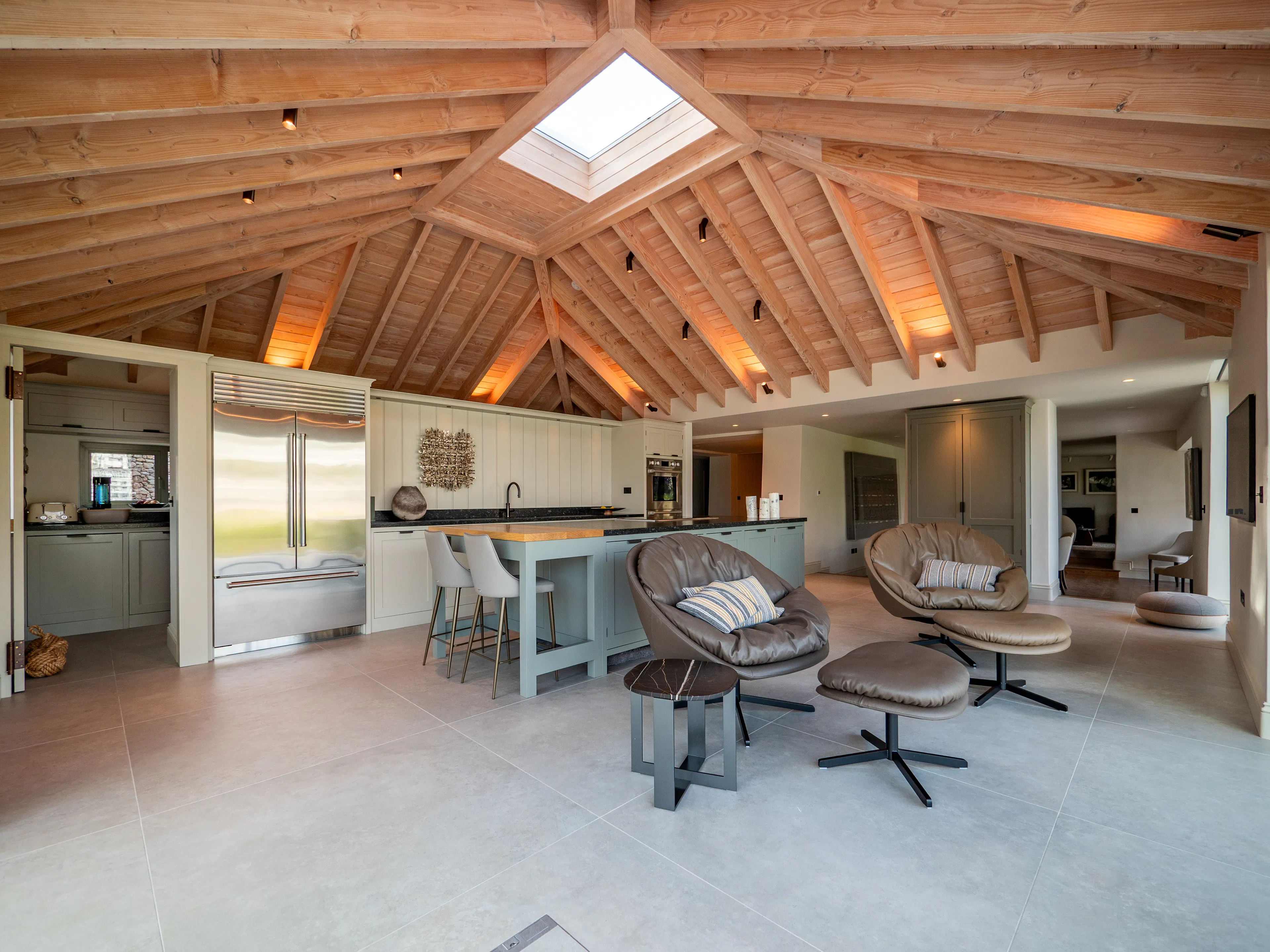 A contemporary Douglas fir glulam framed kitchen extension with a large kitchen island and modern armchairs
