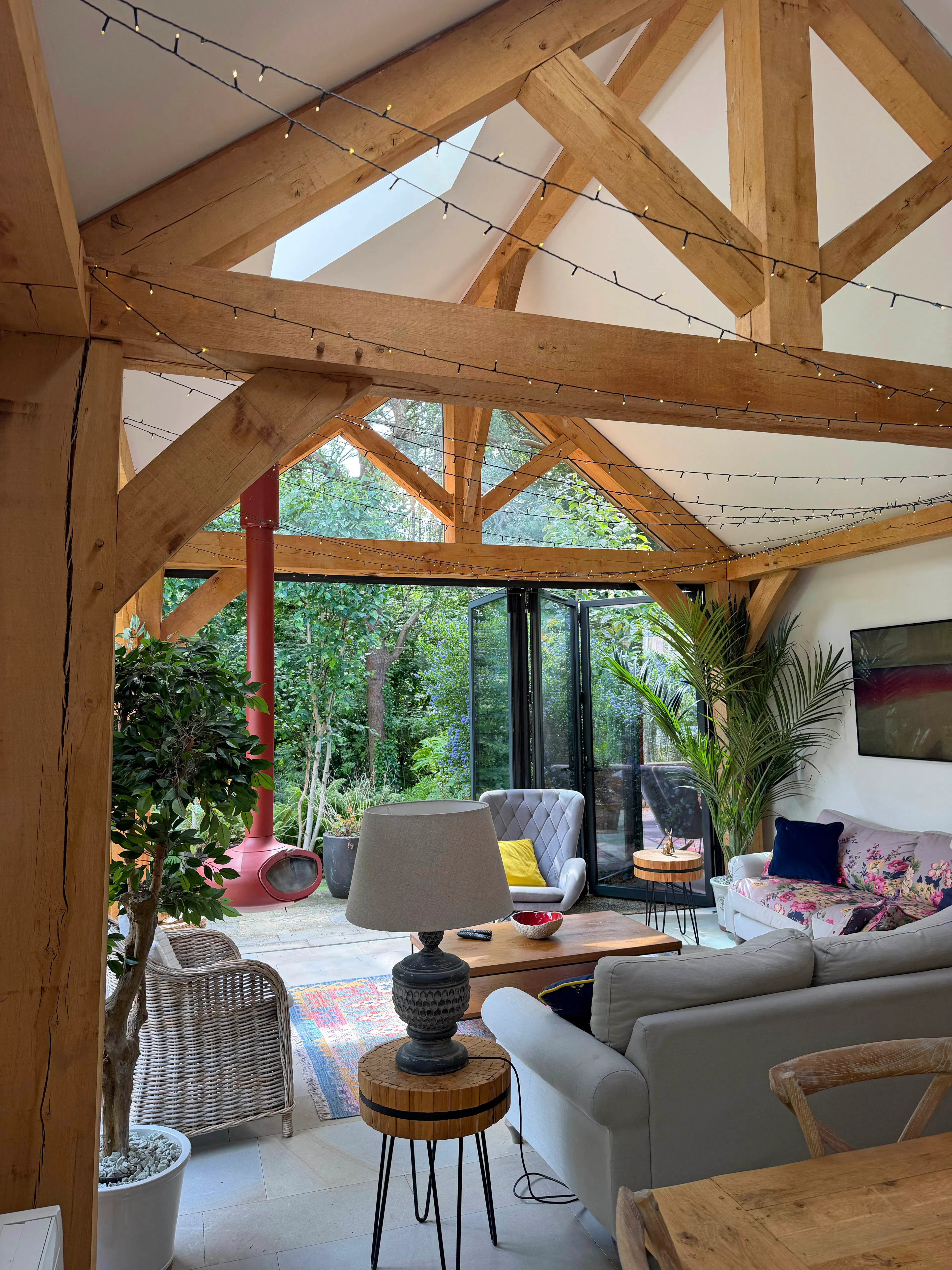 Open-plan garden room interior with exposed oak frame construction and a king post truss, featuring a comfortable lounge seating area within a bright living space