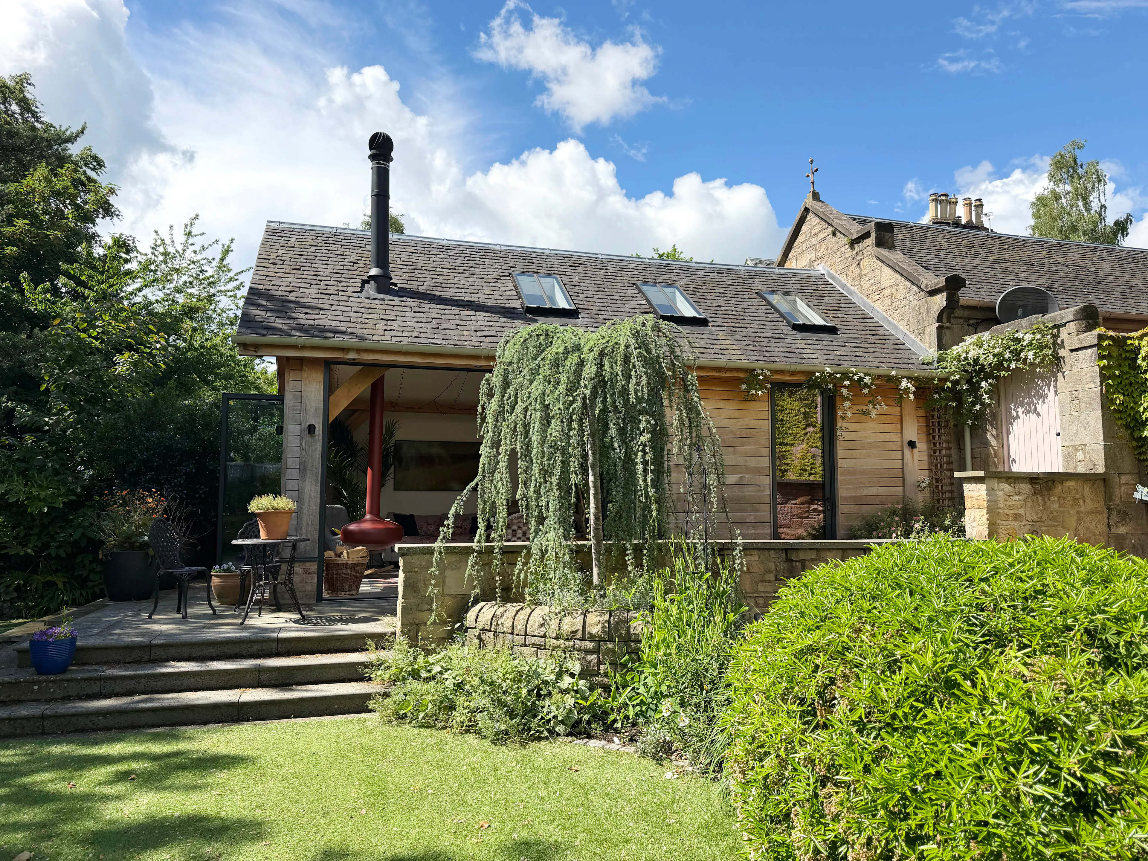 Garden room with oak frame construction, full-width bifold doors, timber cladding, slate roof, and Velux roof windows, viewed from the garden