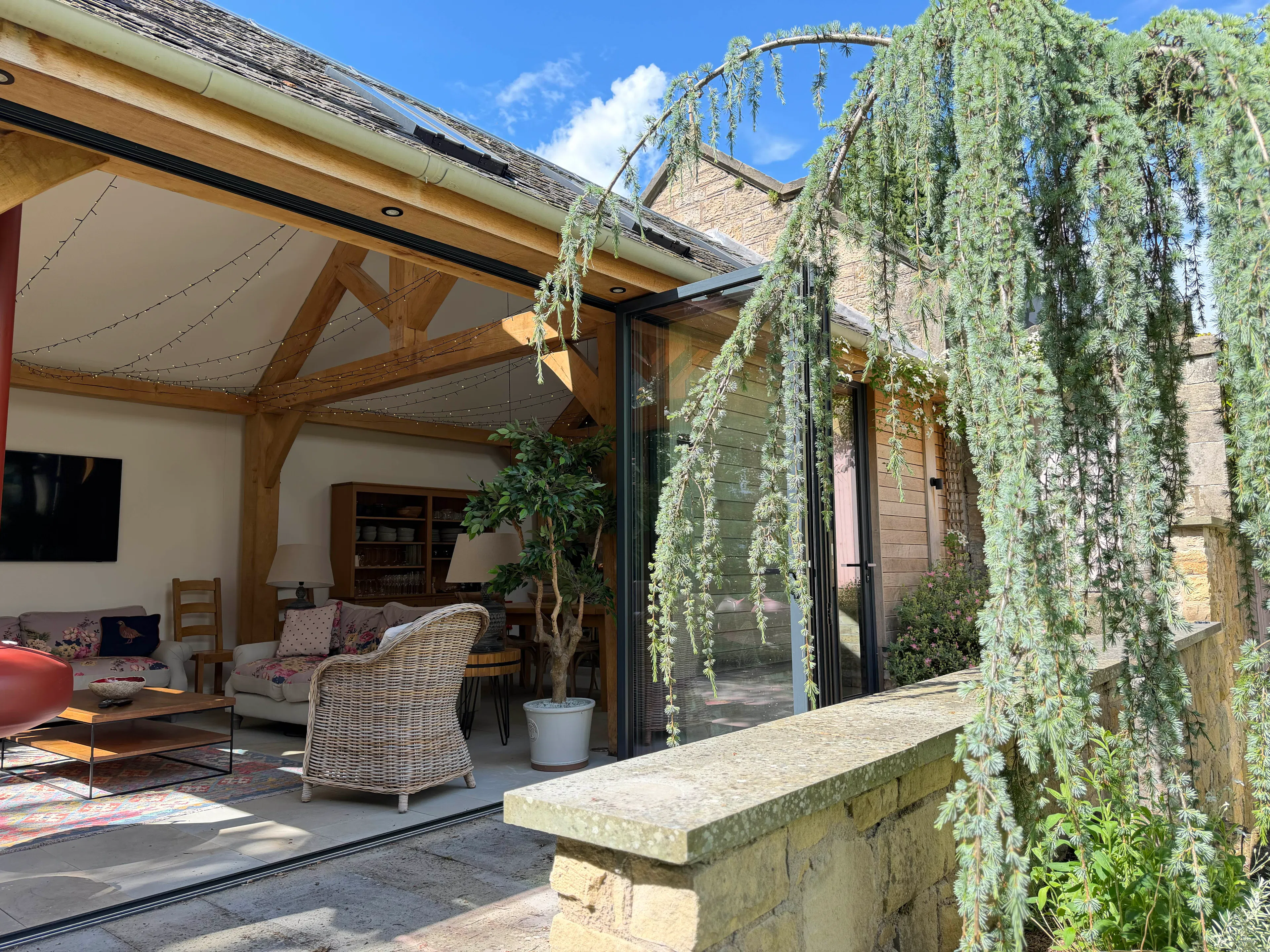 Oak-framed garden room with large bifold doors, set within a landscaped garden with surrounding planting