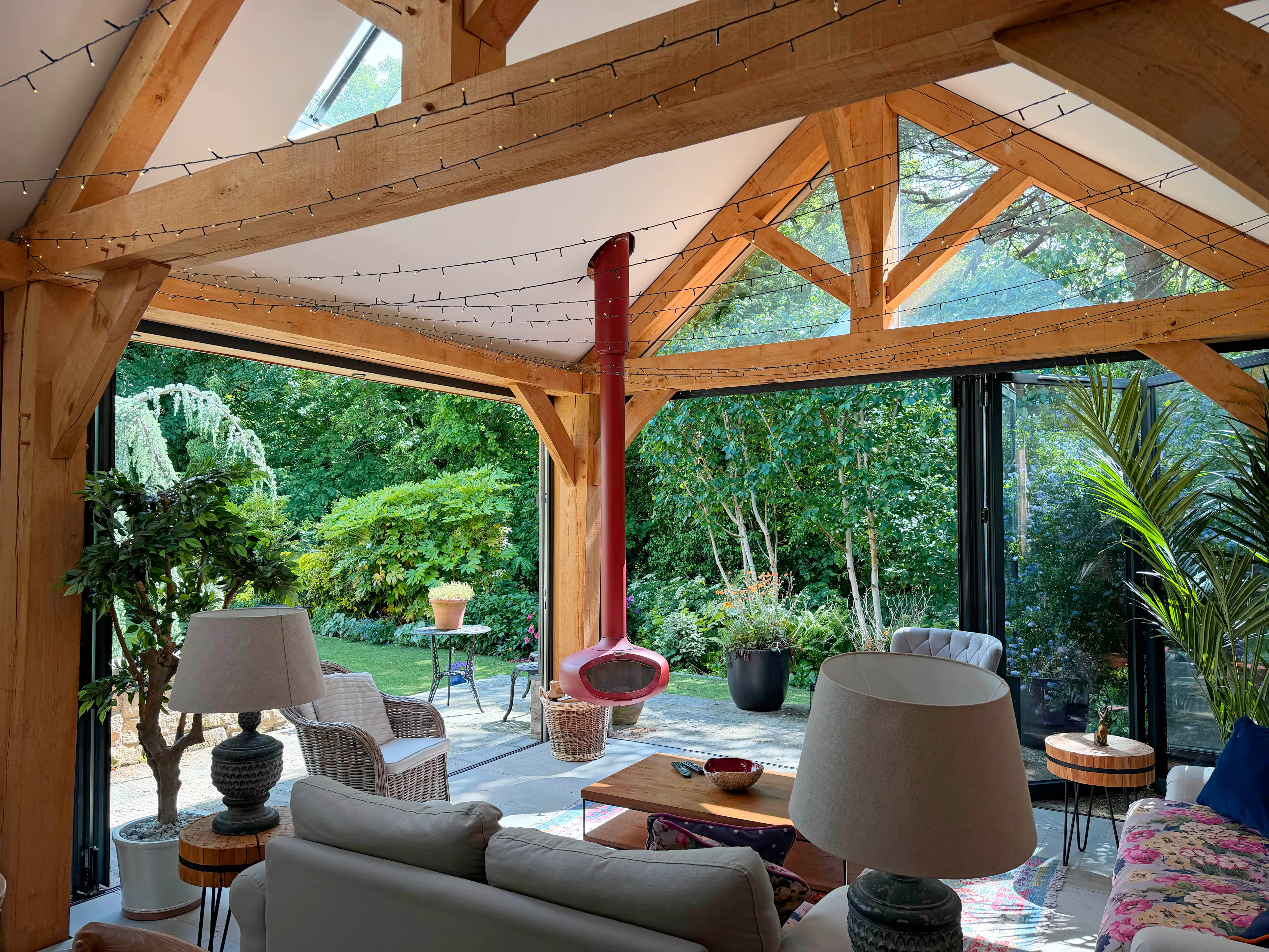 Garden room interior with exposed oak frame construction, featuring a king post truss, structural oak post, fireplace, and large glazed openings that fill the living space with natural light