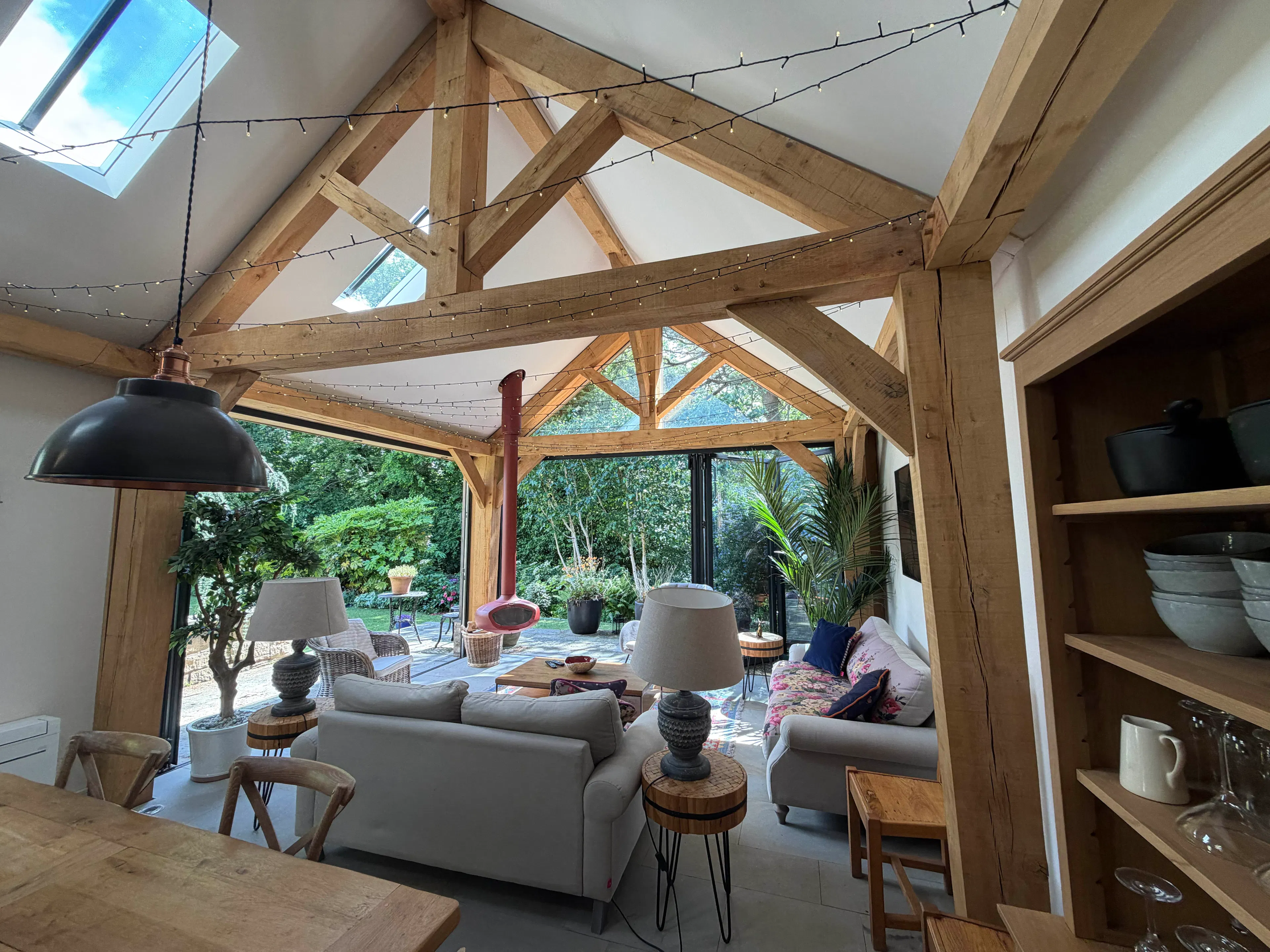 Open-plan garden room interior with exposed oak frame construction, featuring integrated living, kitchen, and dining areas