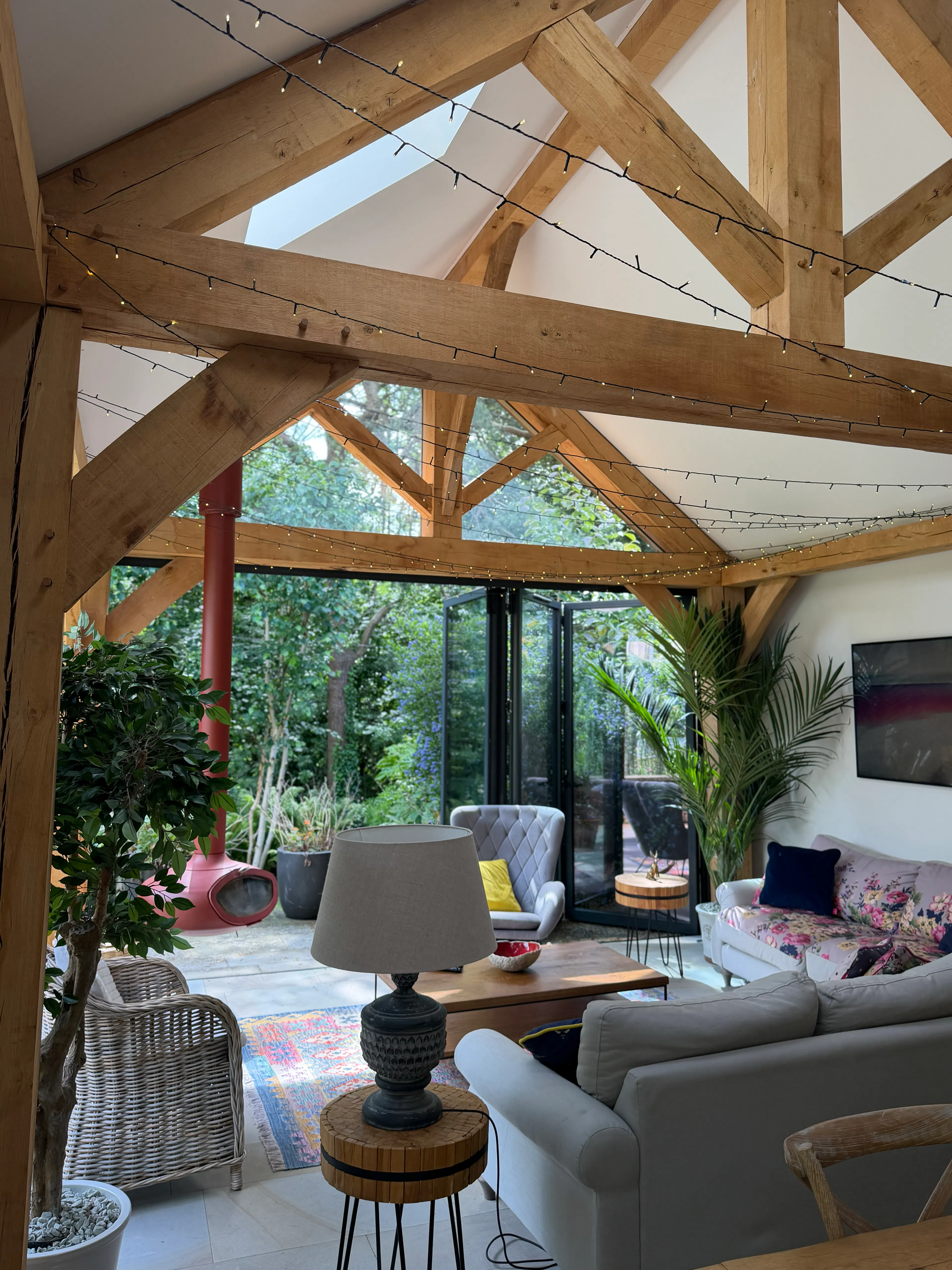 Open-plan garden room interior with exposed oak frame construction and a king post truss, featuring a lounge area within a bright living space