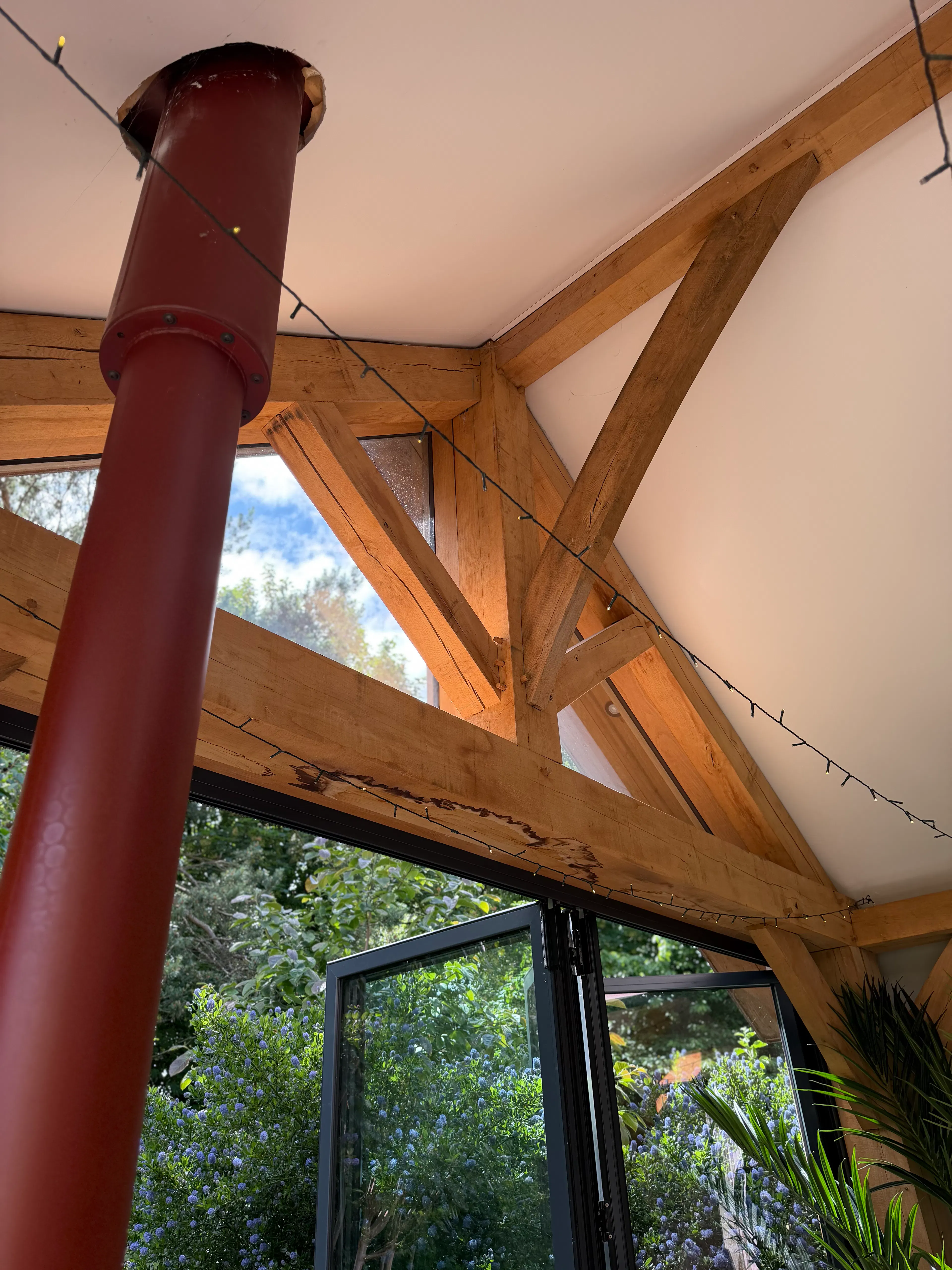 Open-plan garden room interior with exposed oak frame construction and a king post truss, featuring extensive glazing that fills the living space with natural light