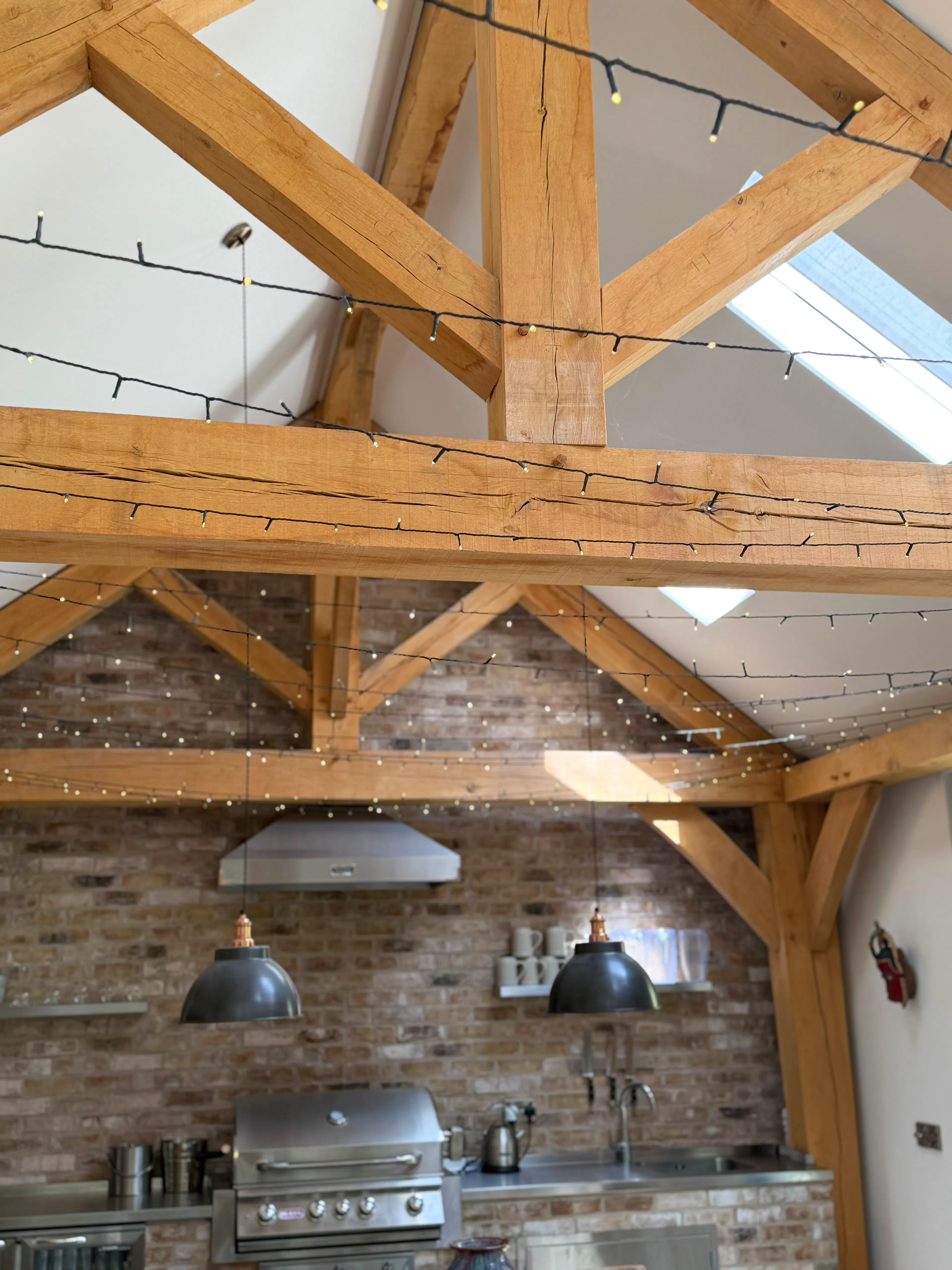 Interior garden room with exposed oak frame construction and a king post truss, showing detailed views of the kitchen area within the open-plan space