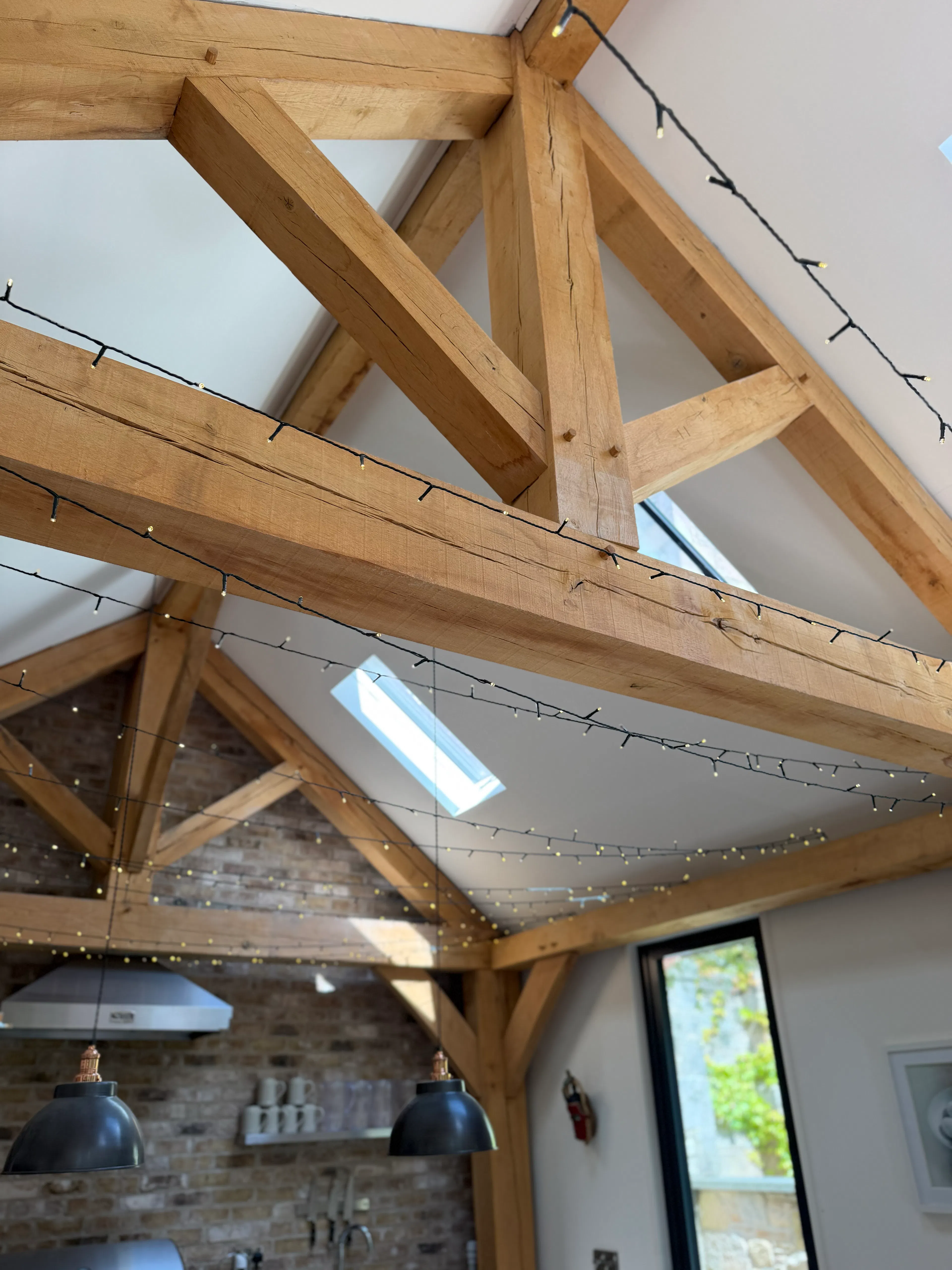 Interior garden room with exposed oak frame construction, featuring a king post truss and detailed close-up of structural post connections and timber joinery