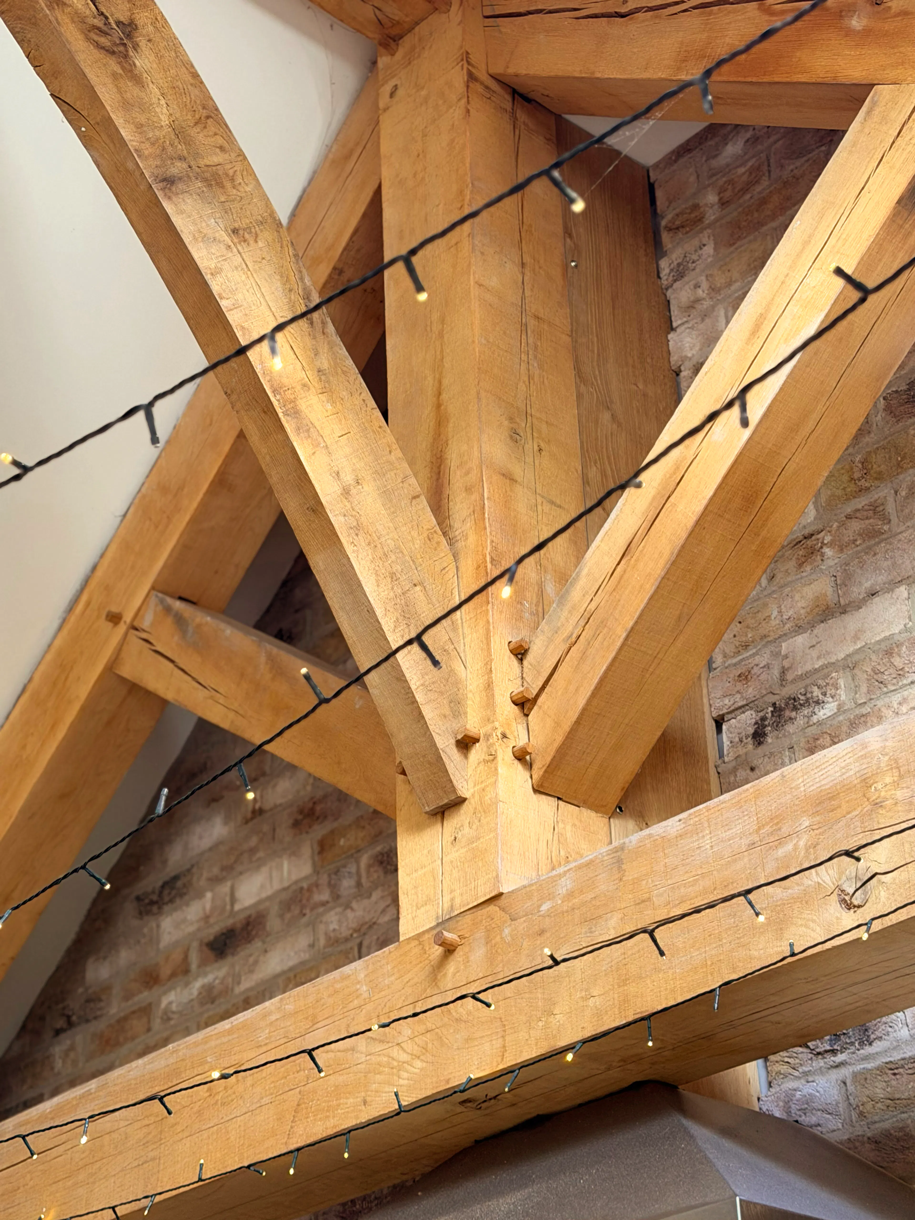 Interior garden room with exposed oak frame construction and a king post truss, featuring a close-up view of detailed timber joinery connections