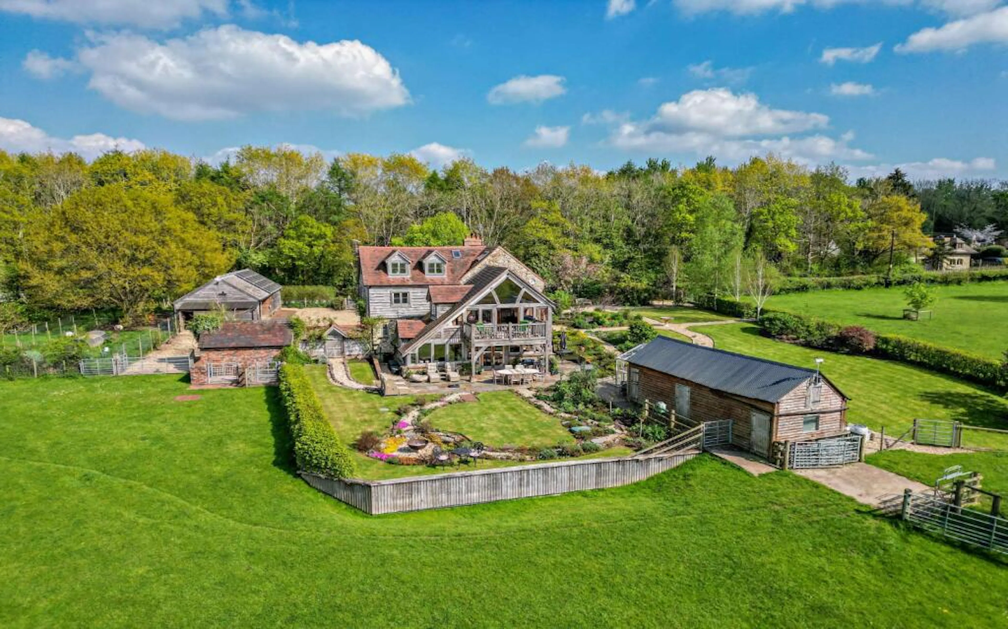 A landscaped garden in front of a traditional stone cottage with a red tile roof and oak framed extension