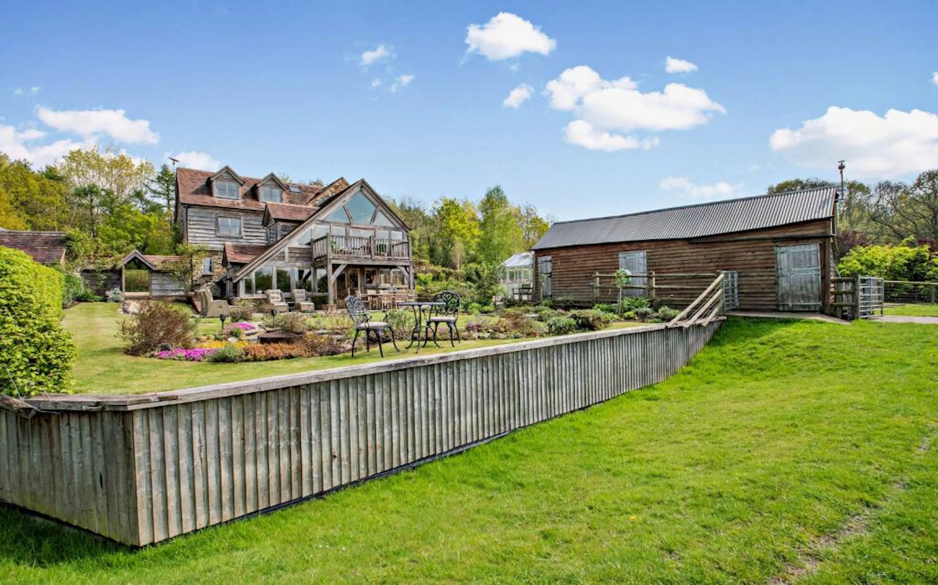 A landscaped garden in front of a traditional stone cottage with a red tile roof and oak framed extension
