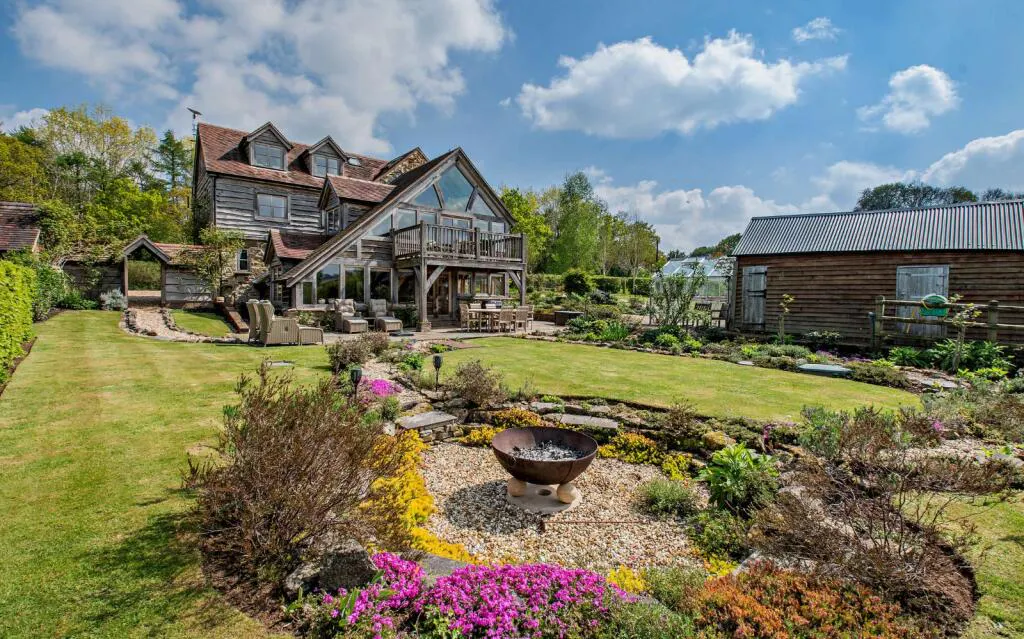 A landscaped garden with a firepit in front of a traditional stone cottage with a red tile roof and oak framed extension