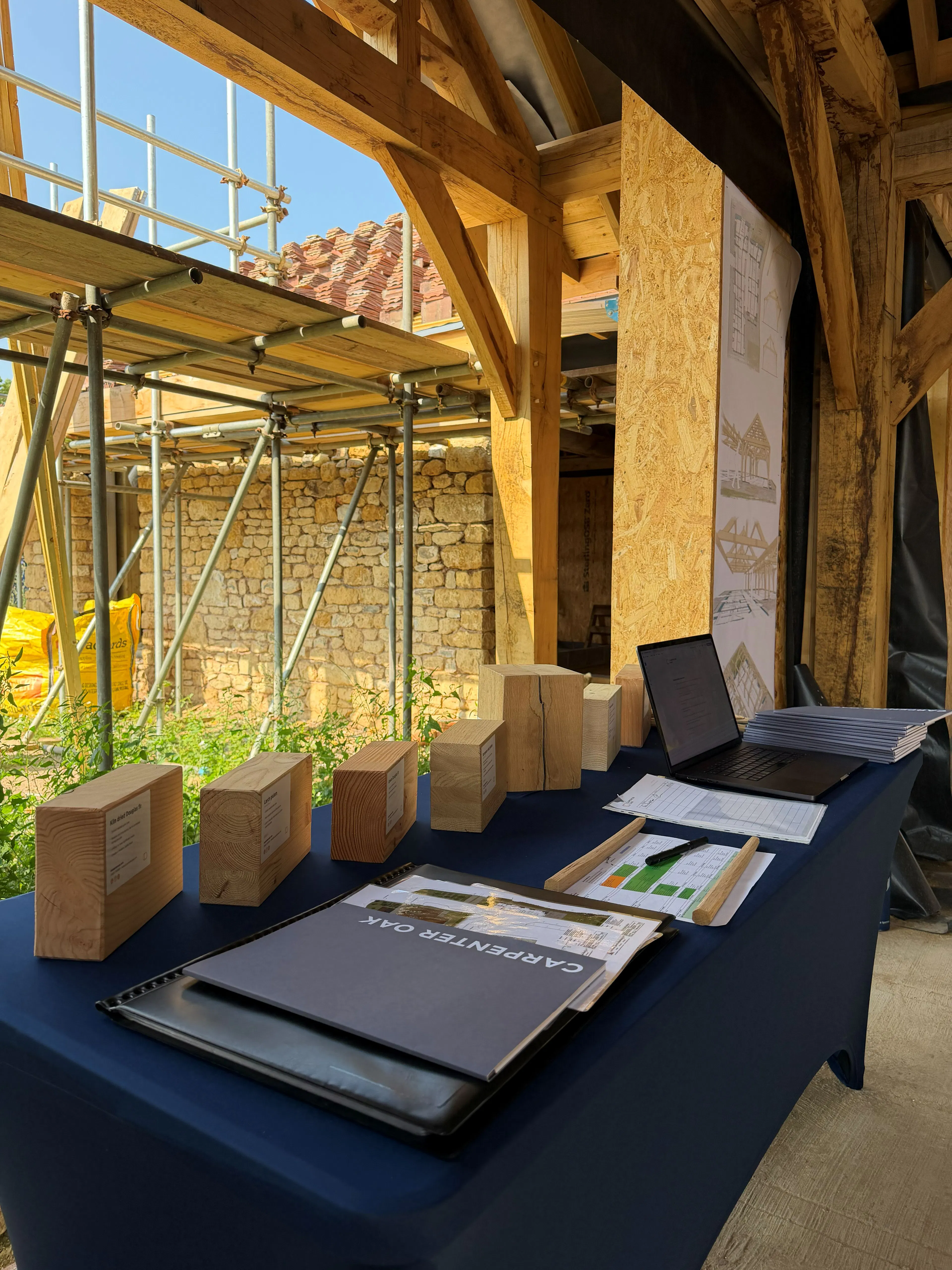 A table with marketing materials and timber samples at an event on a construction site of an oak frame house mid-build