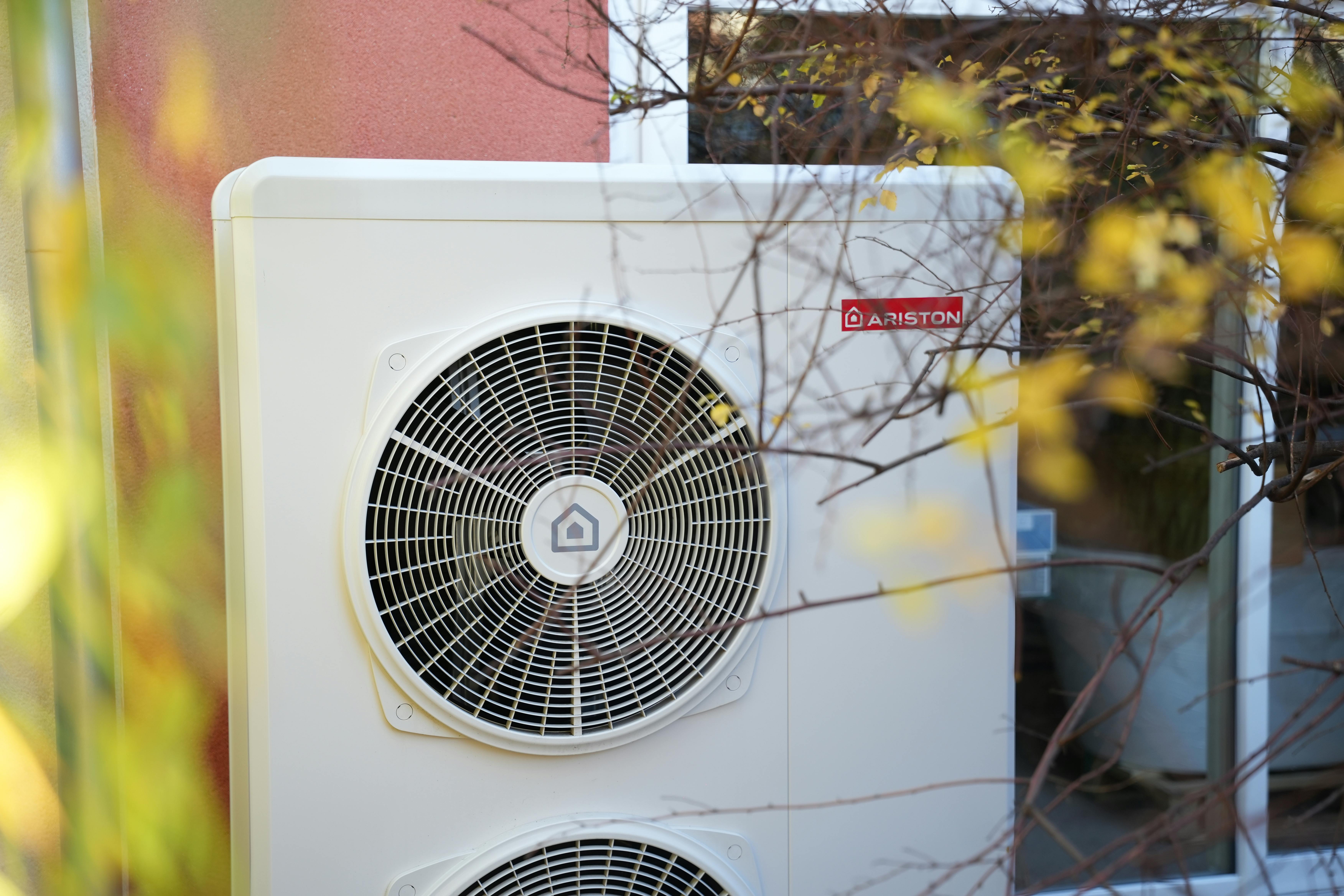 Pompe à chaleur air eau de marque Ariston installée face à un mur de maison