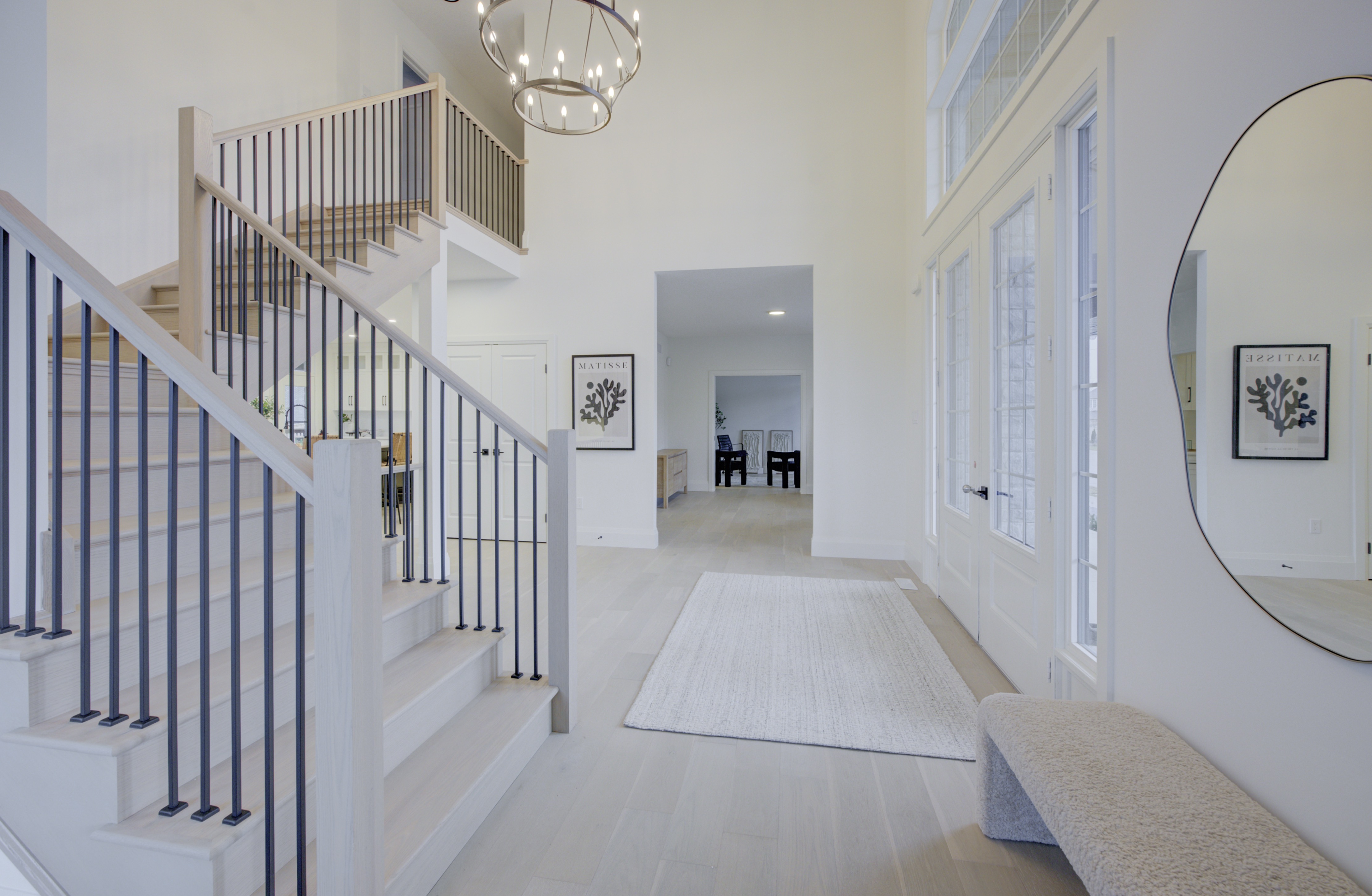 Bright modern foyer with a staircase, large round mirror, and chandelier, leading to an open hallway