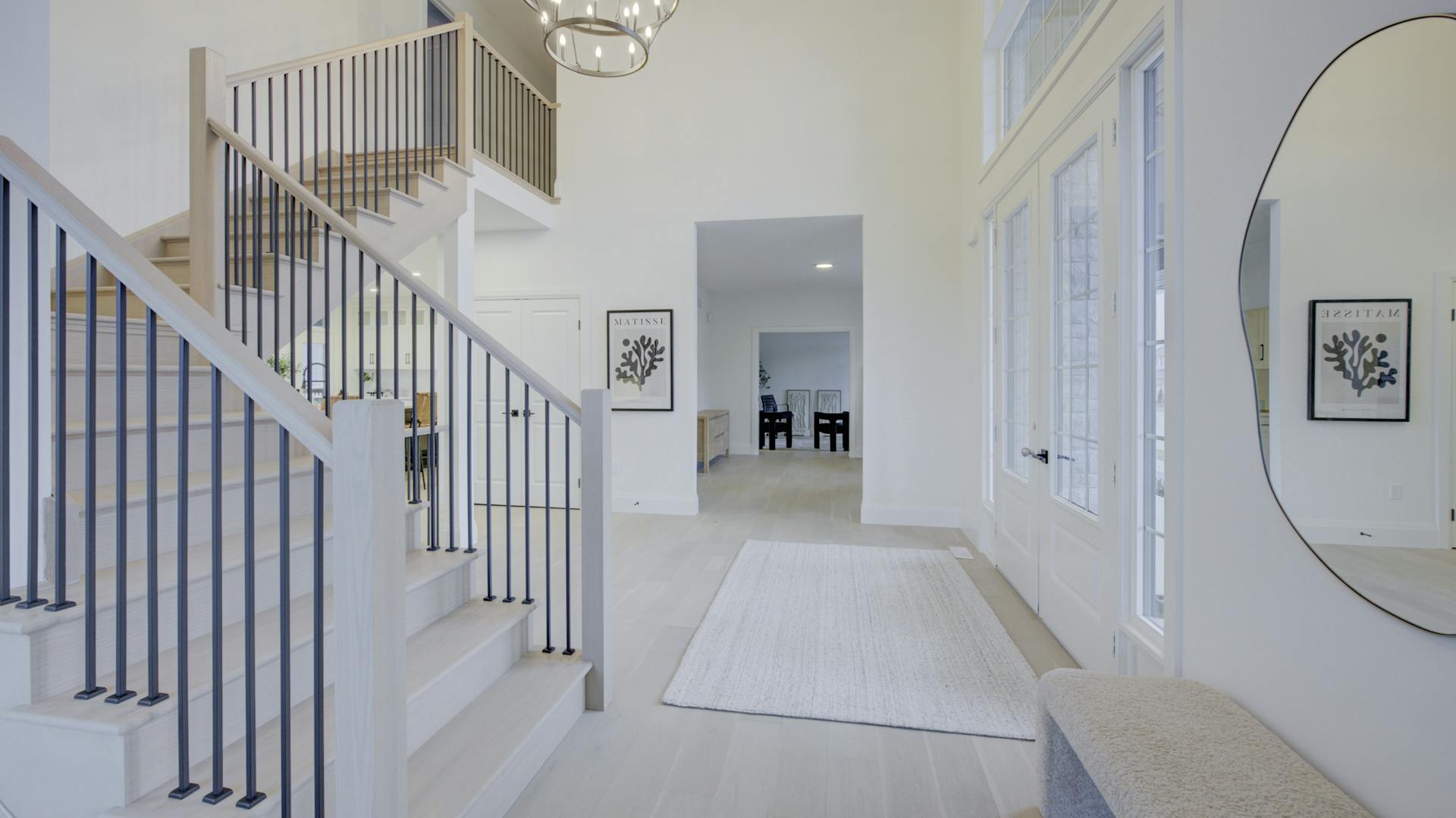 Bright modern foyer with a staircase, large round mirror, and chandelier, leading to an open hallway