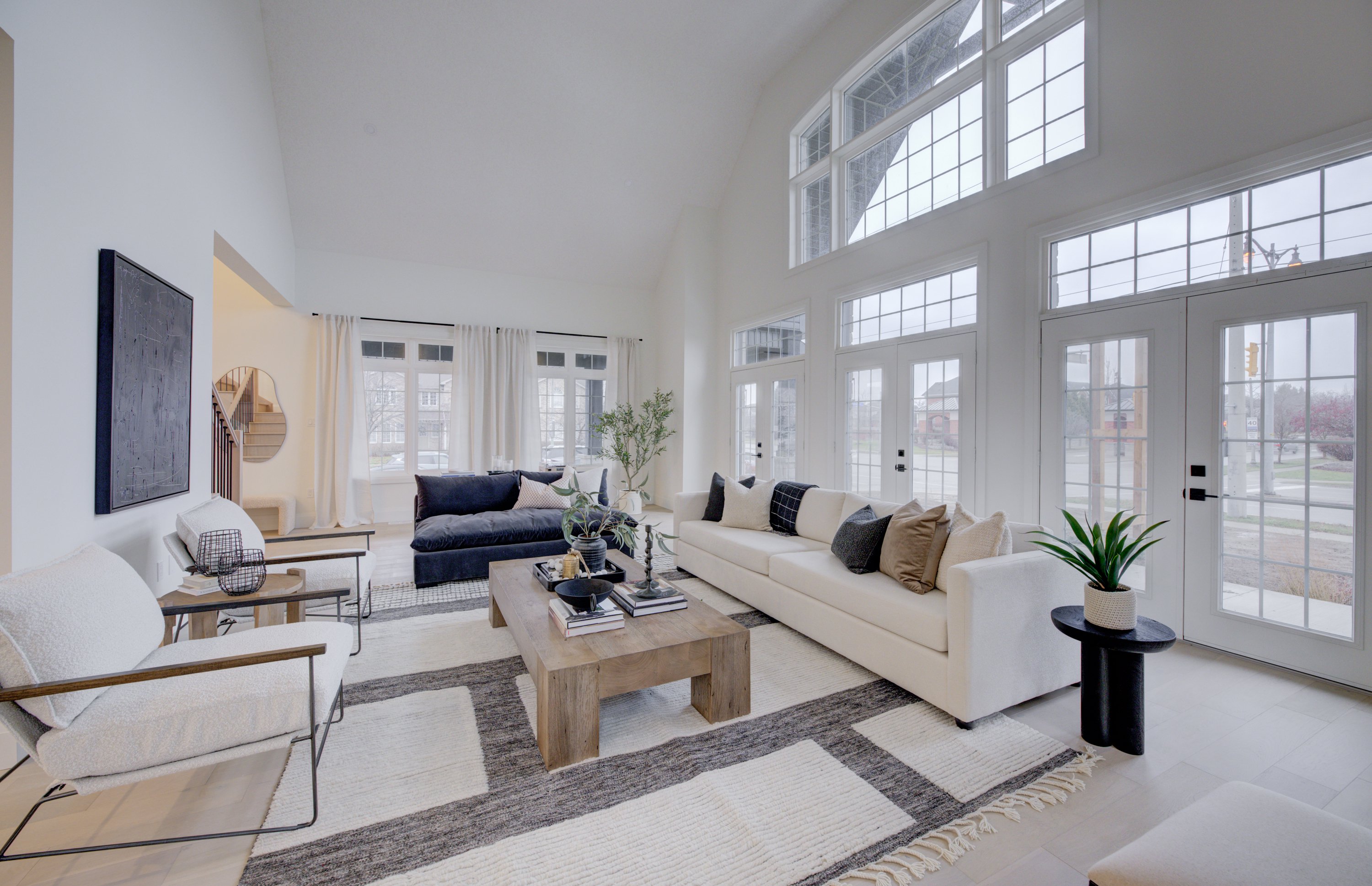 Spacious living room with high ceilings, large windows, neutral sofas, and a wood coffee table
