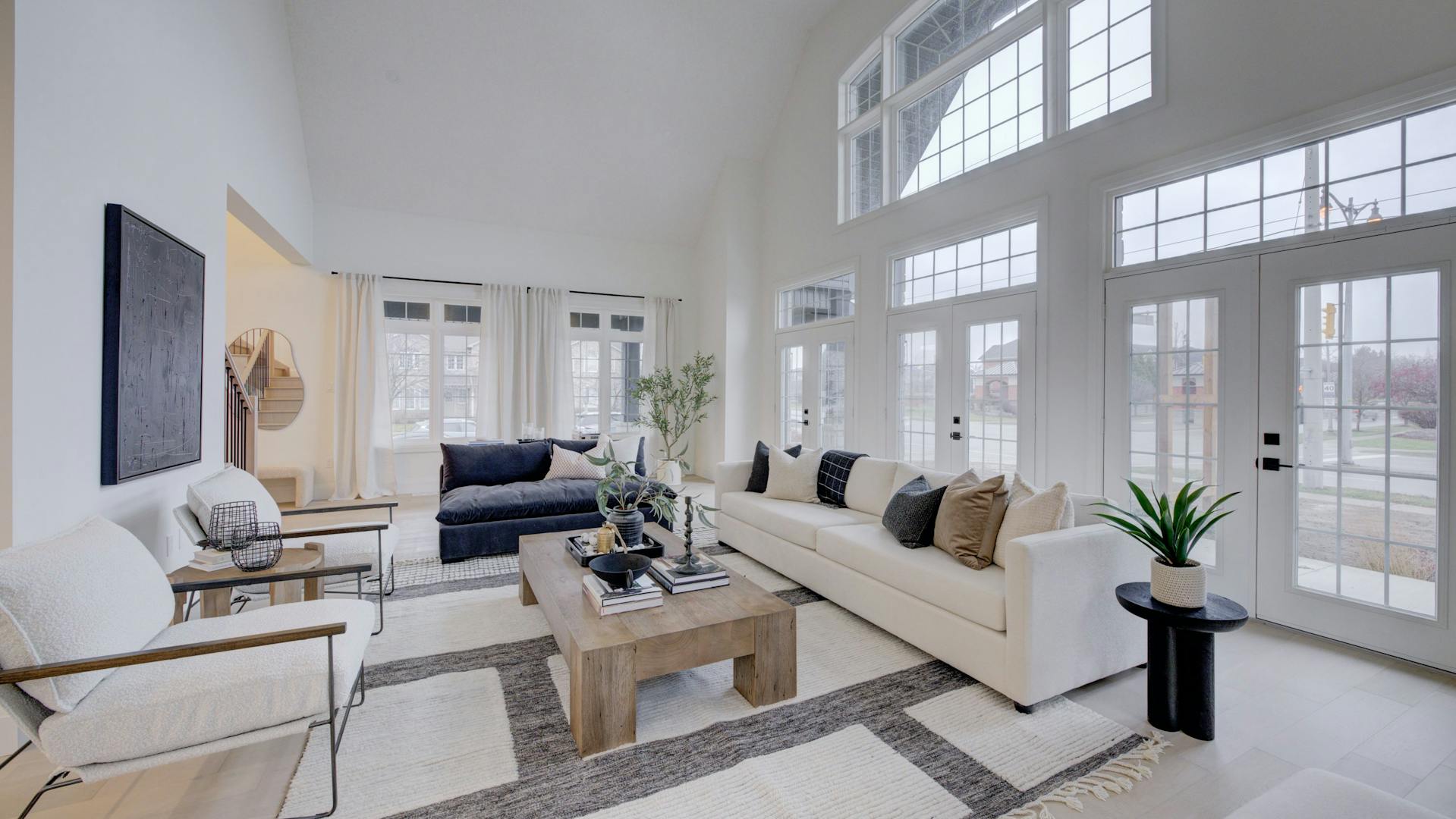Spacious living room with high ceilings, large windows, neutral sofas, and a wood coffee table