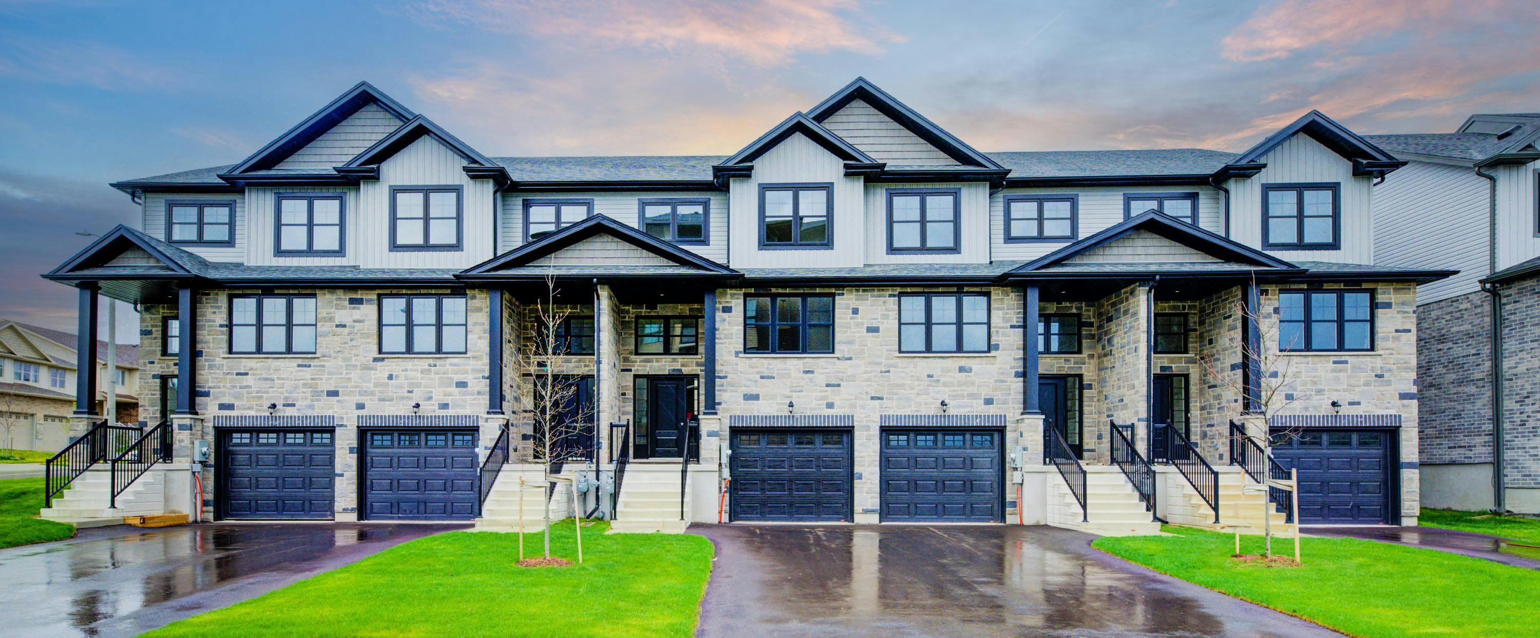 Modern stone and siding townhomes with black accents, gabled rooflines, and individual garages