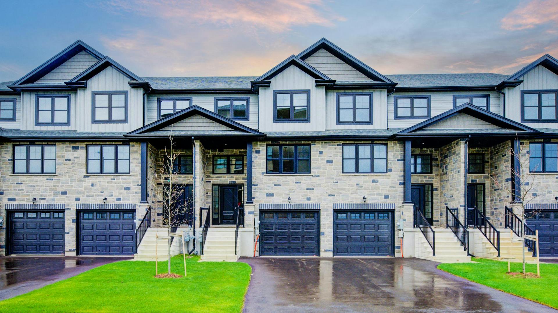 Modern stone and siding townhomes with black accents, gabled rooflines, and individual garages