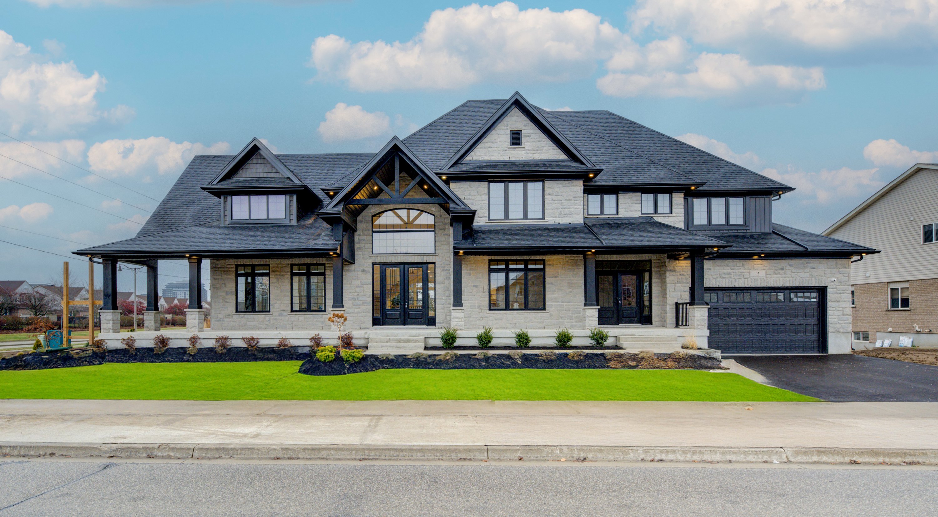 Elegant stone-clad two-story home with black trim, gabled roof, large windows, and a covered front porch