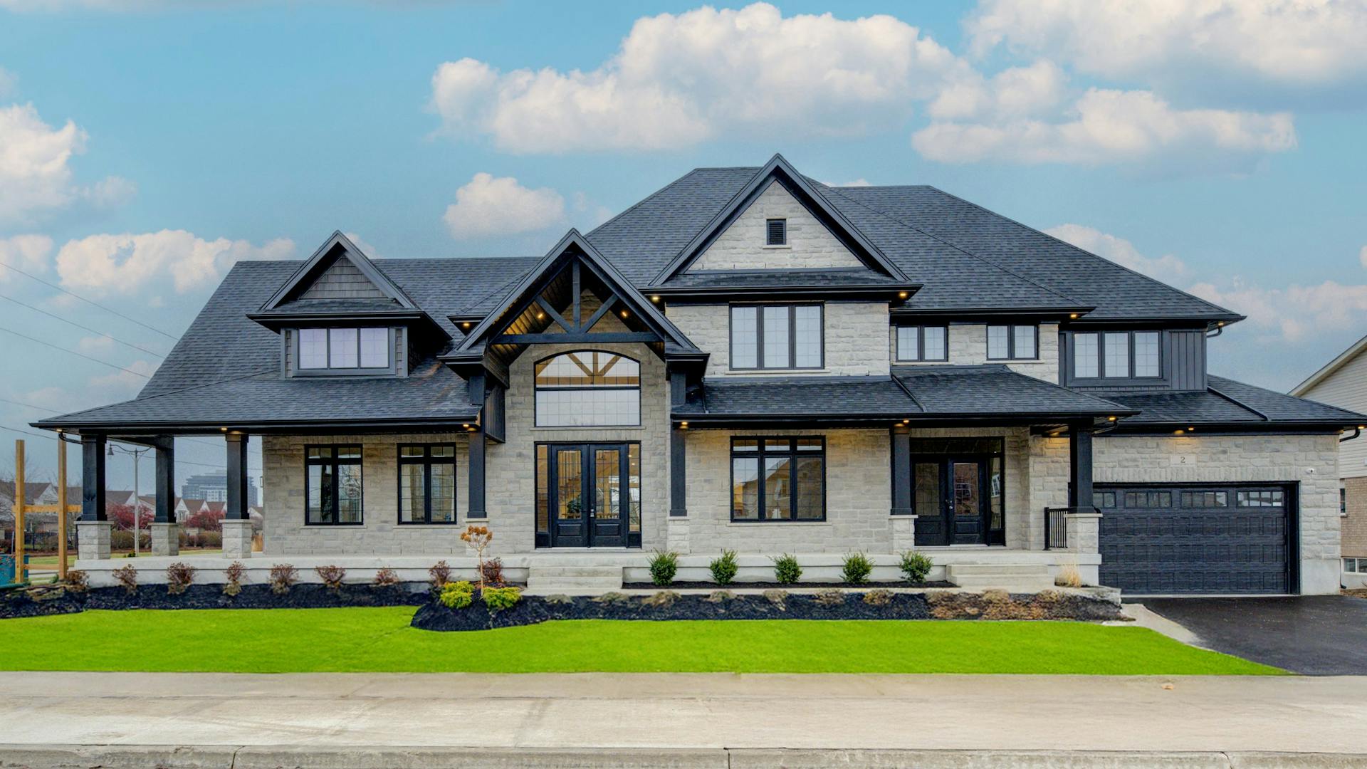 Elegant stone-clad two-story home with black trim, gabled roof, large windows, and a covered front porch