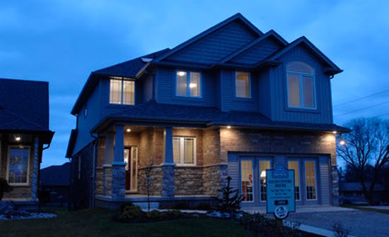 Two-story home at dusk with lights illuminating the stone and siding exterior.