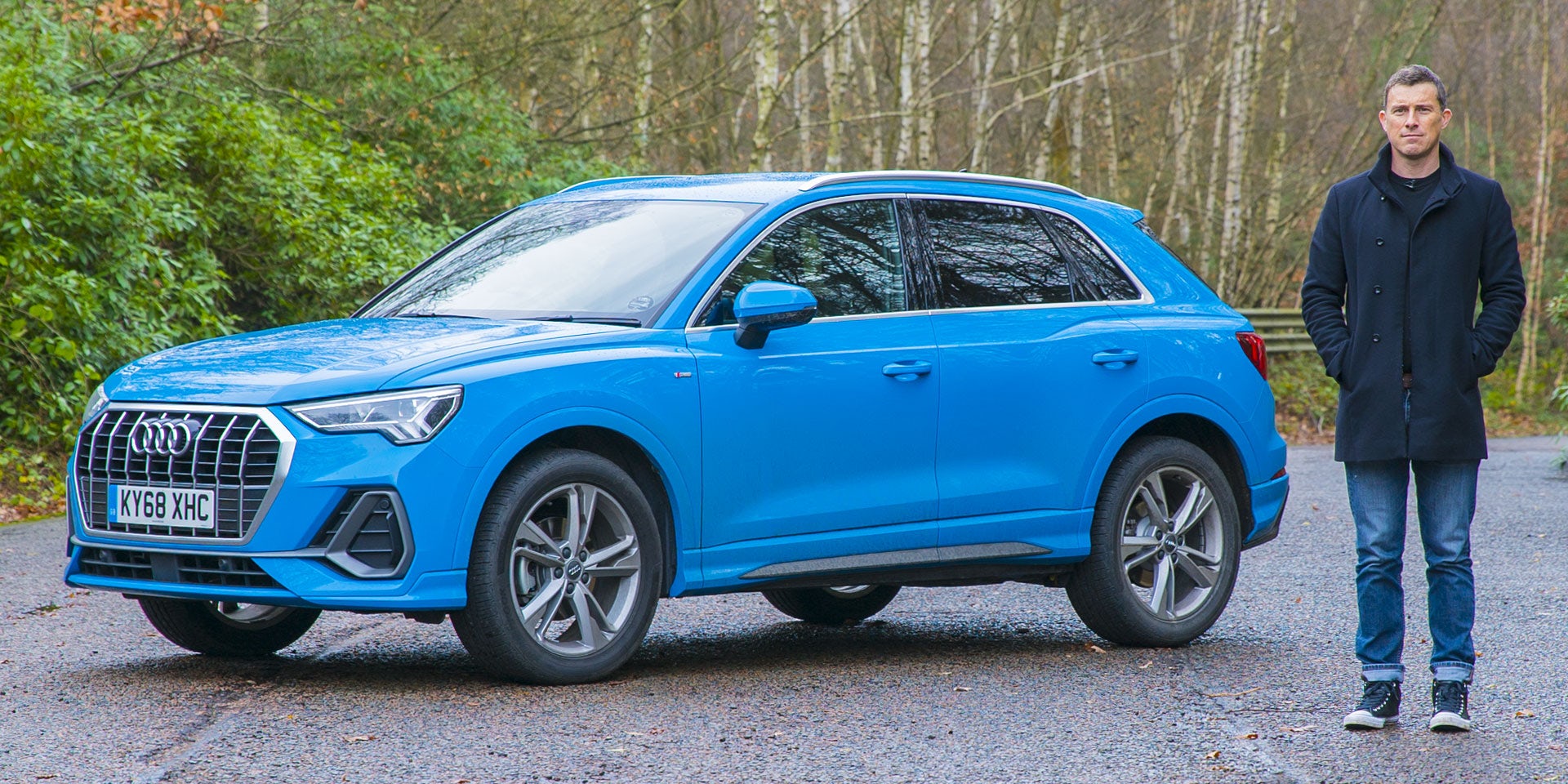 Mat Watson stood next to a blue 2022 Audi Q3 for a video thumbnail.