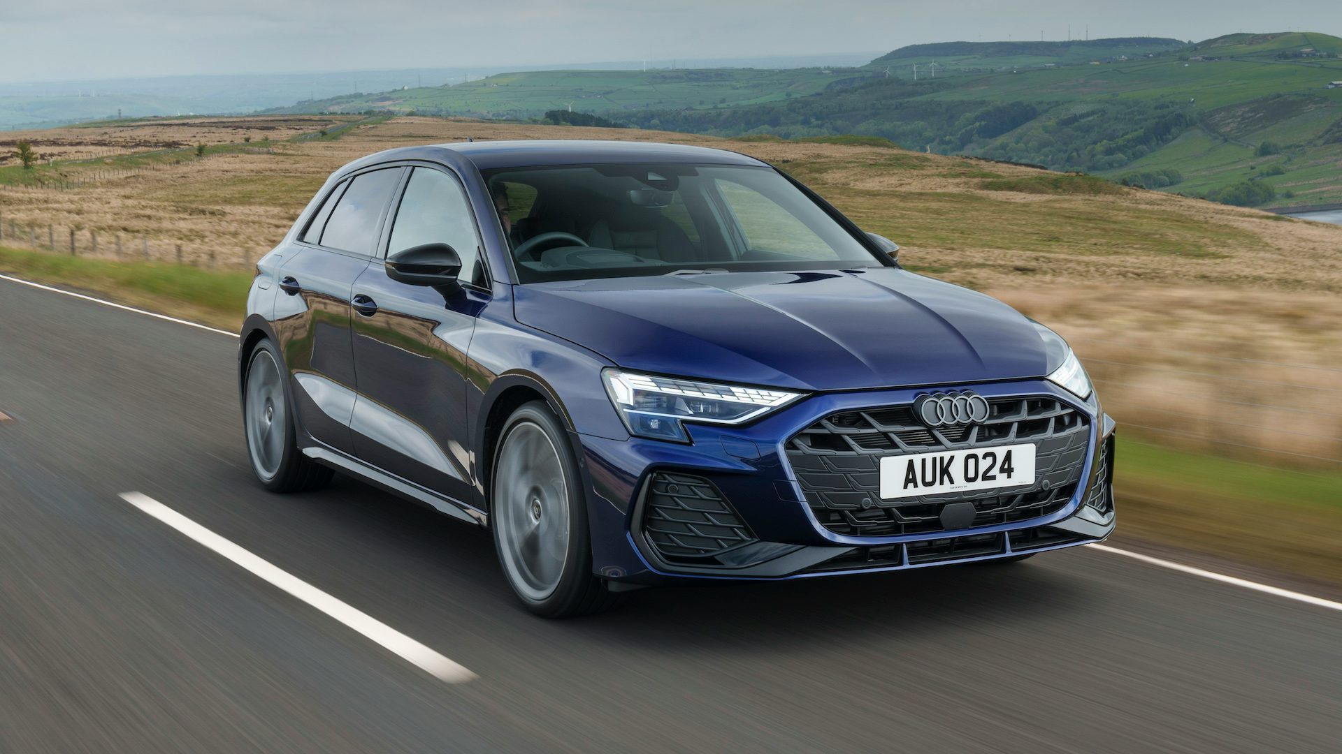 Blue 2024 Audi A3 driving in the countryside, front quarter angle.