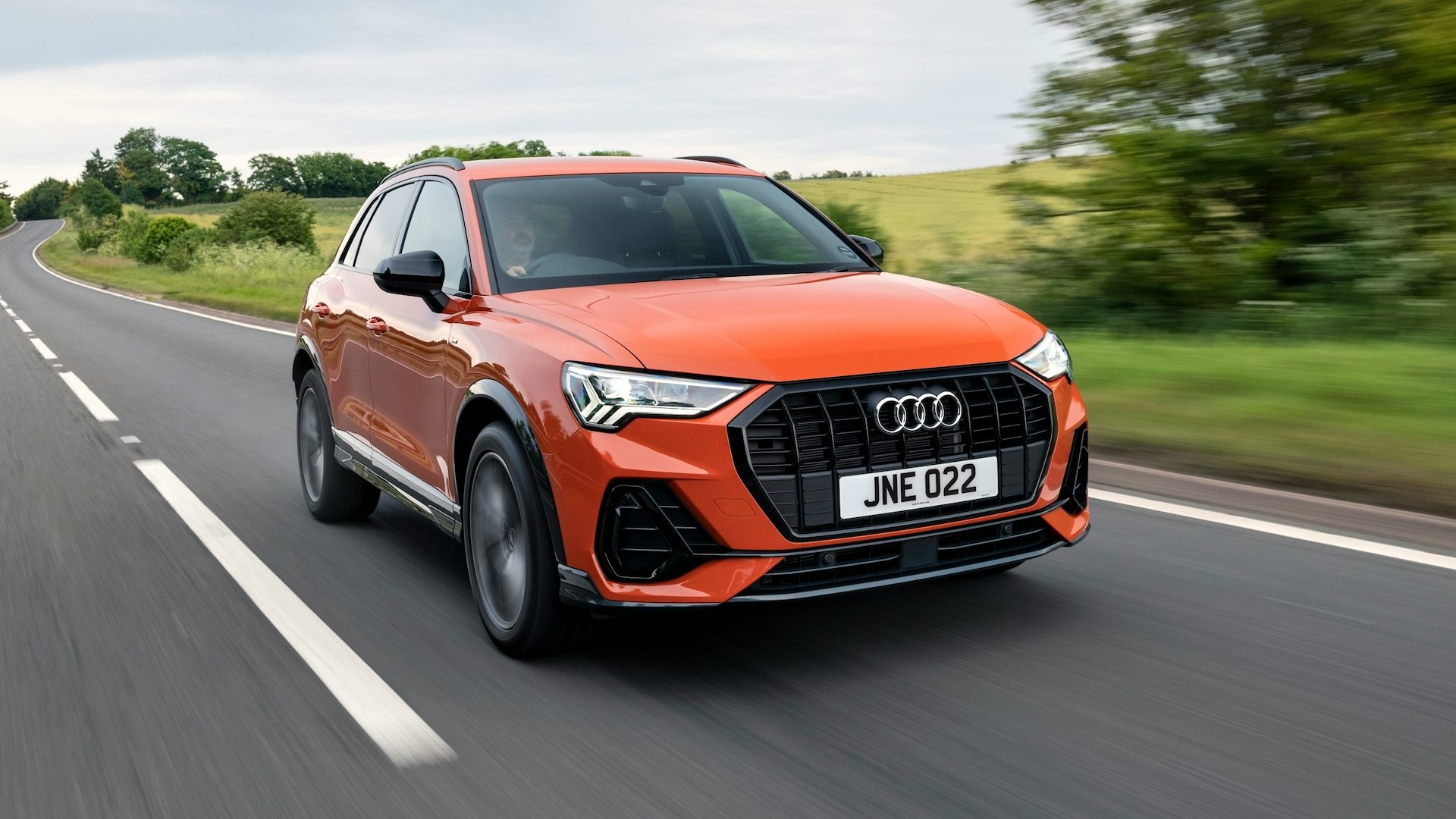 Orange 2022 Audi Q3 driving in the countryside, front quarter view.