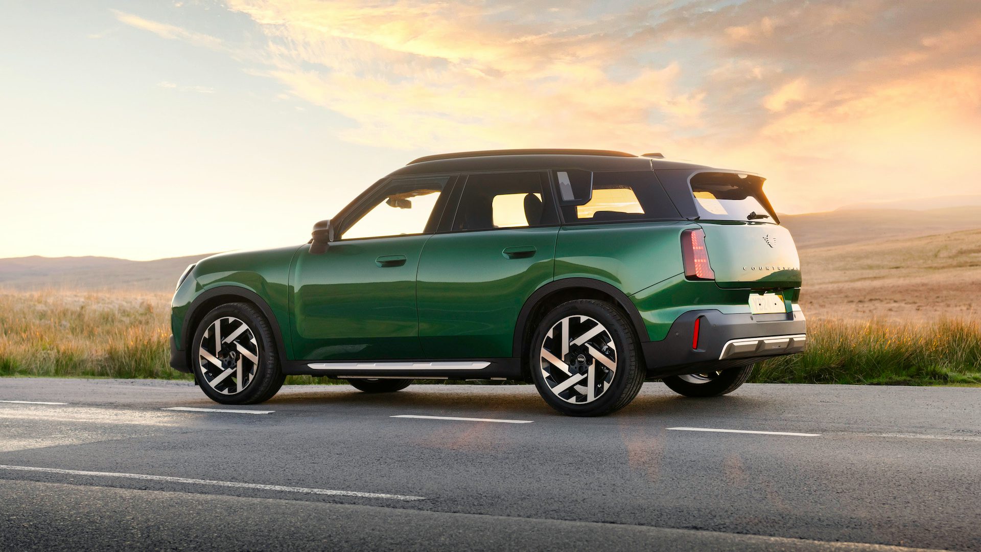 Green 2024 Mini Countryman Electric parked on the road with fields behind at sunset, side view.