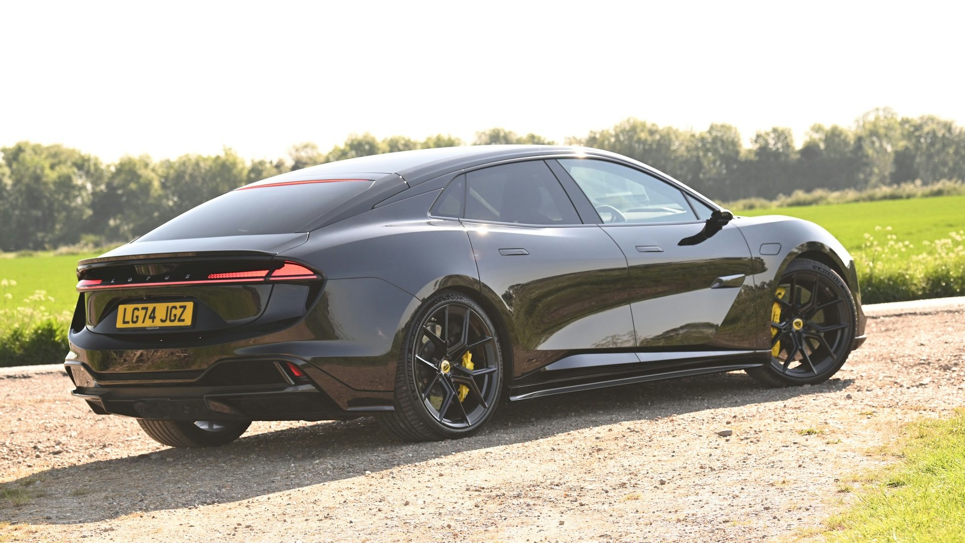 Black 2025 Lotus Emeya parked on gravel, rear quarter view.