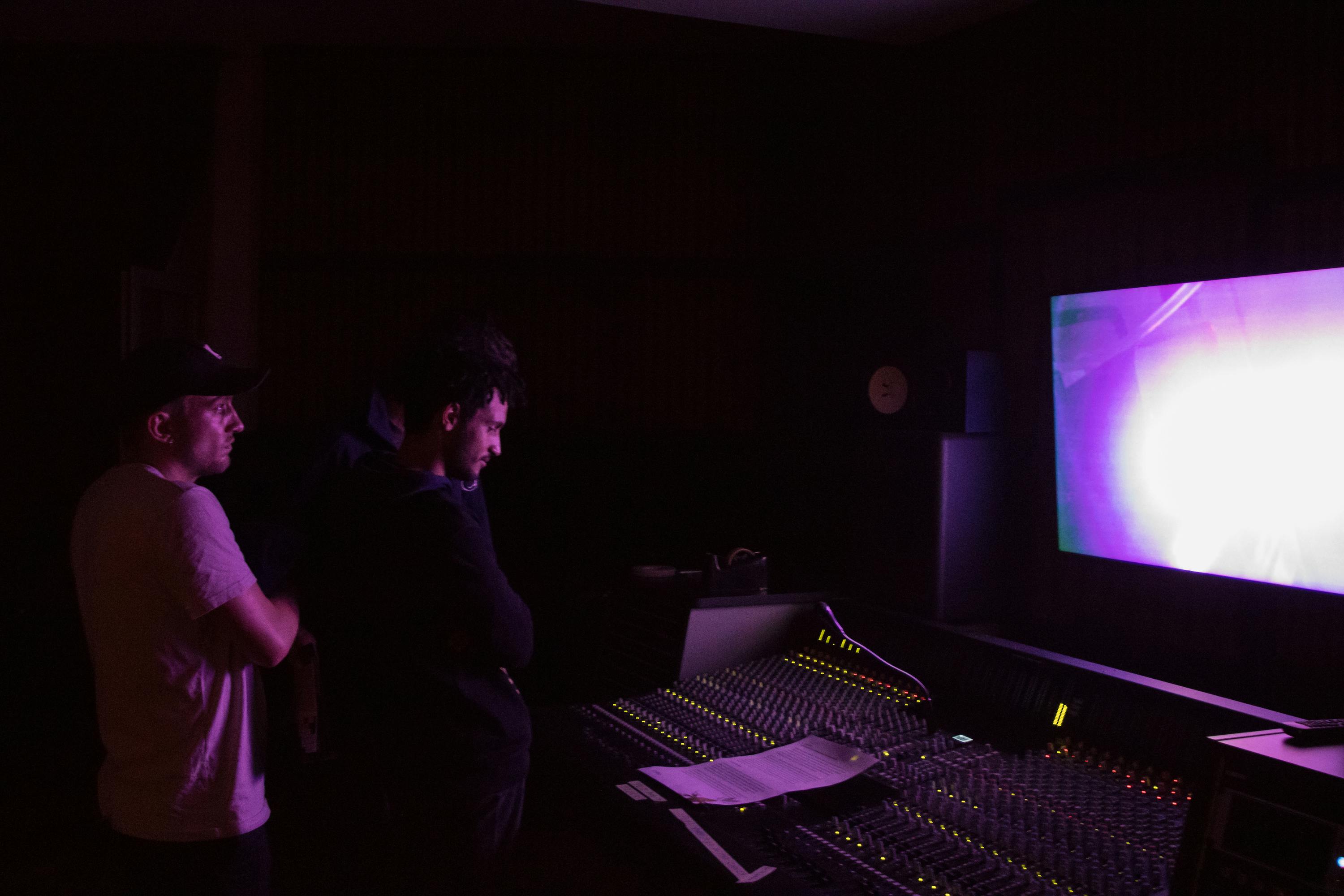Traum Eck (Tamas Marquetant & Sebastian Dürer) 's installation. People in a dark room look at a screen and audio controller. The screen gives off a pink glow