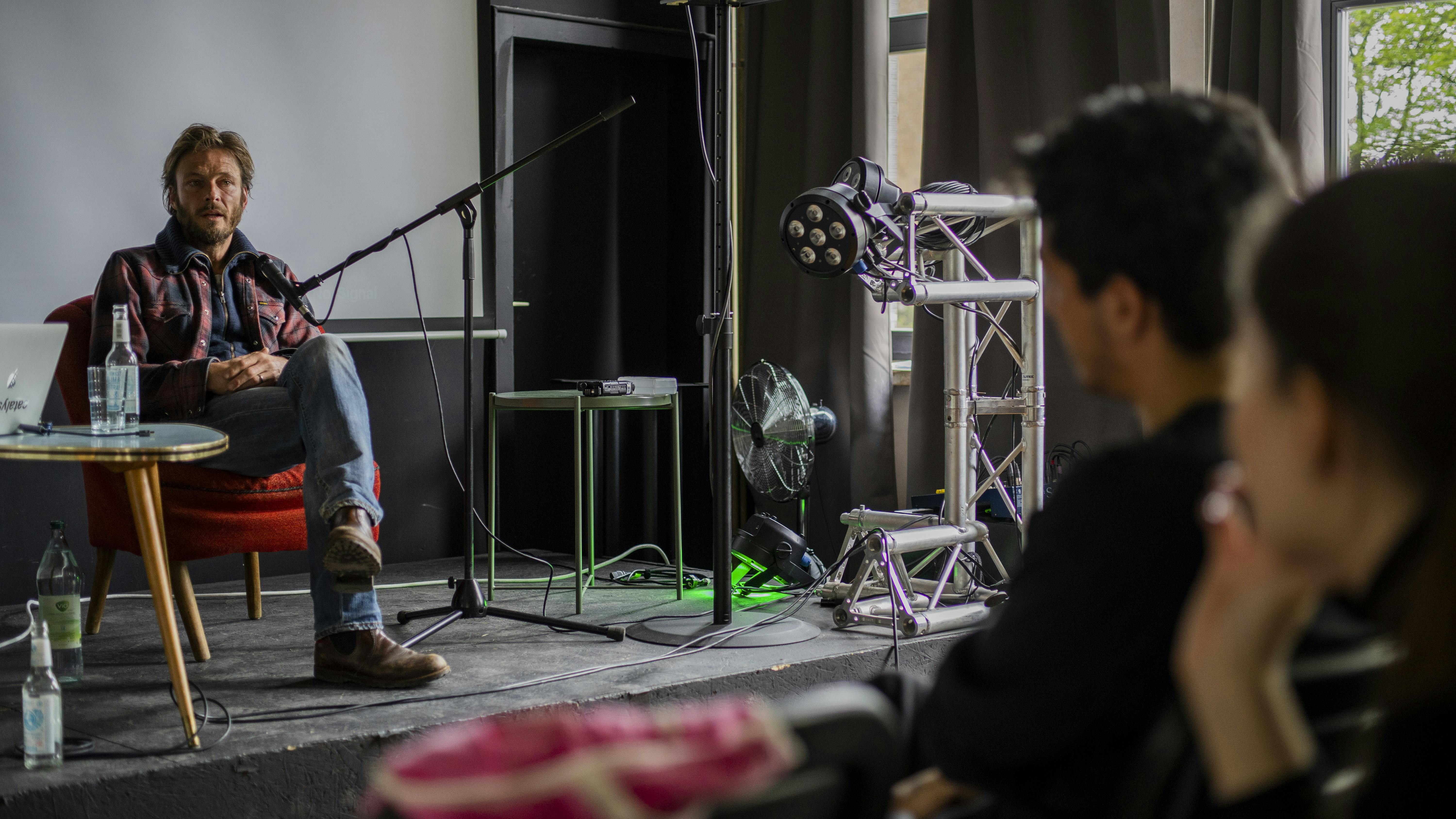 Andreas Pietschmann sits on stage, he is relaxed. In front of him is an audience of students.