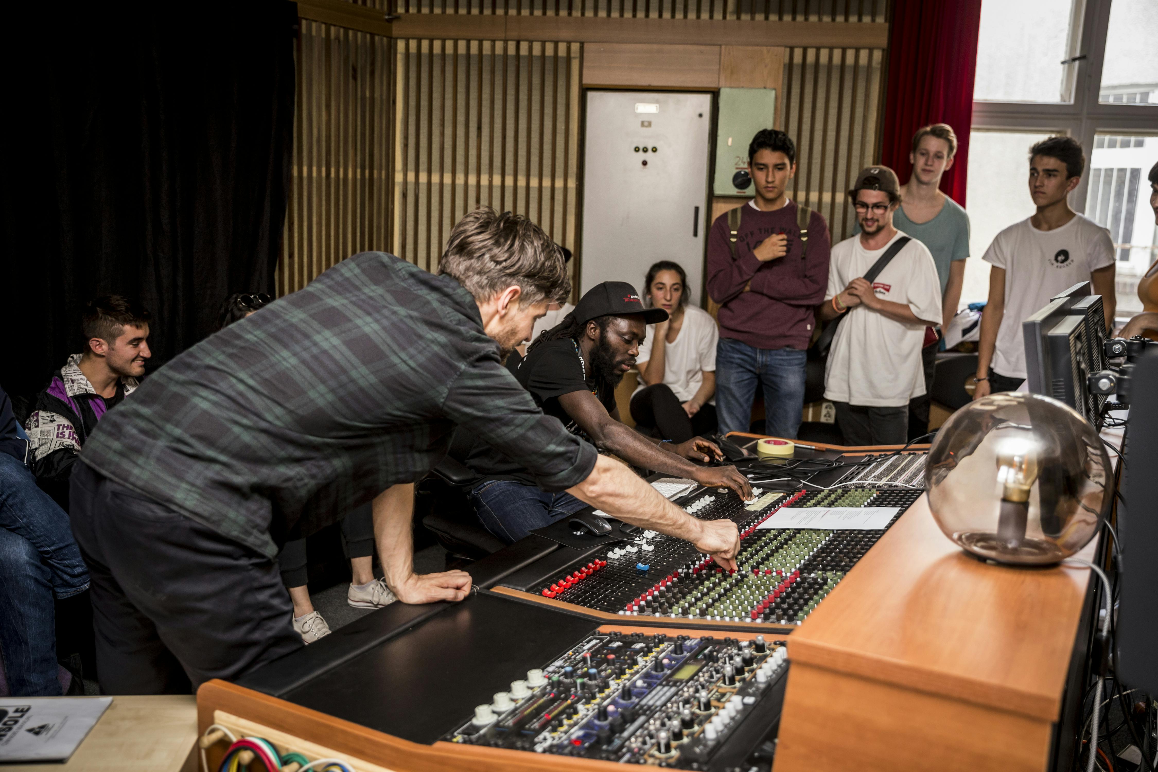 Tutor and guest adjusts levels on the mixing deck while students take note