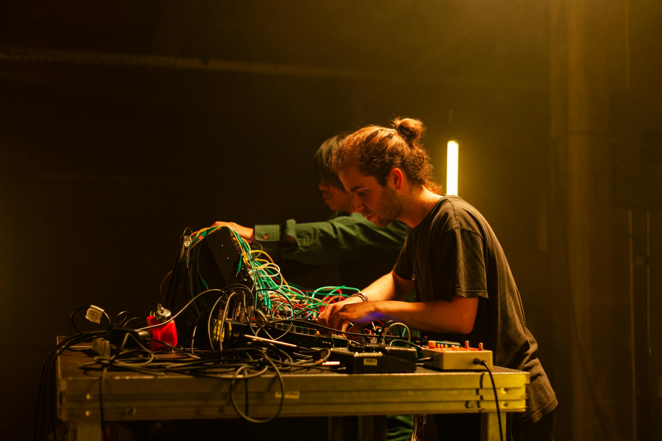 students in a performance using modular synthesisers, midi keyboards and instruments. the stage is lit yellow