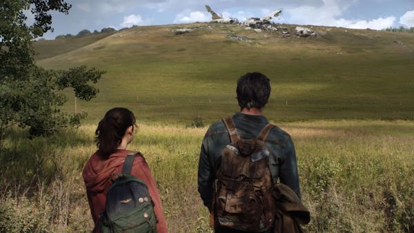 two people look onto the site of a plane crash on a hill in the distance