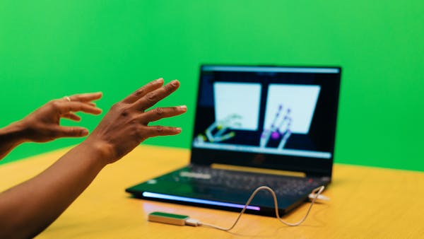 two hands infront of a laptop are represented live on the laptop screen through motion sensors
