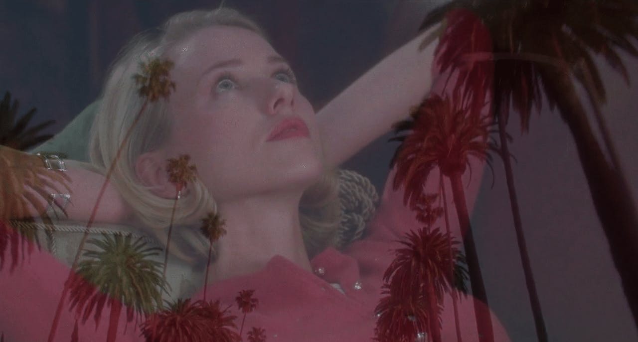 A woman in a pink dress peacefully rests on a bed, overlayed palm trees providing a serene backdrop.