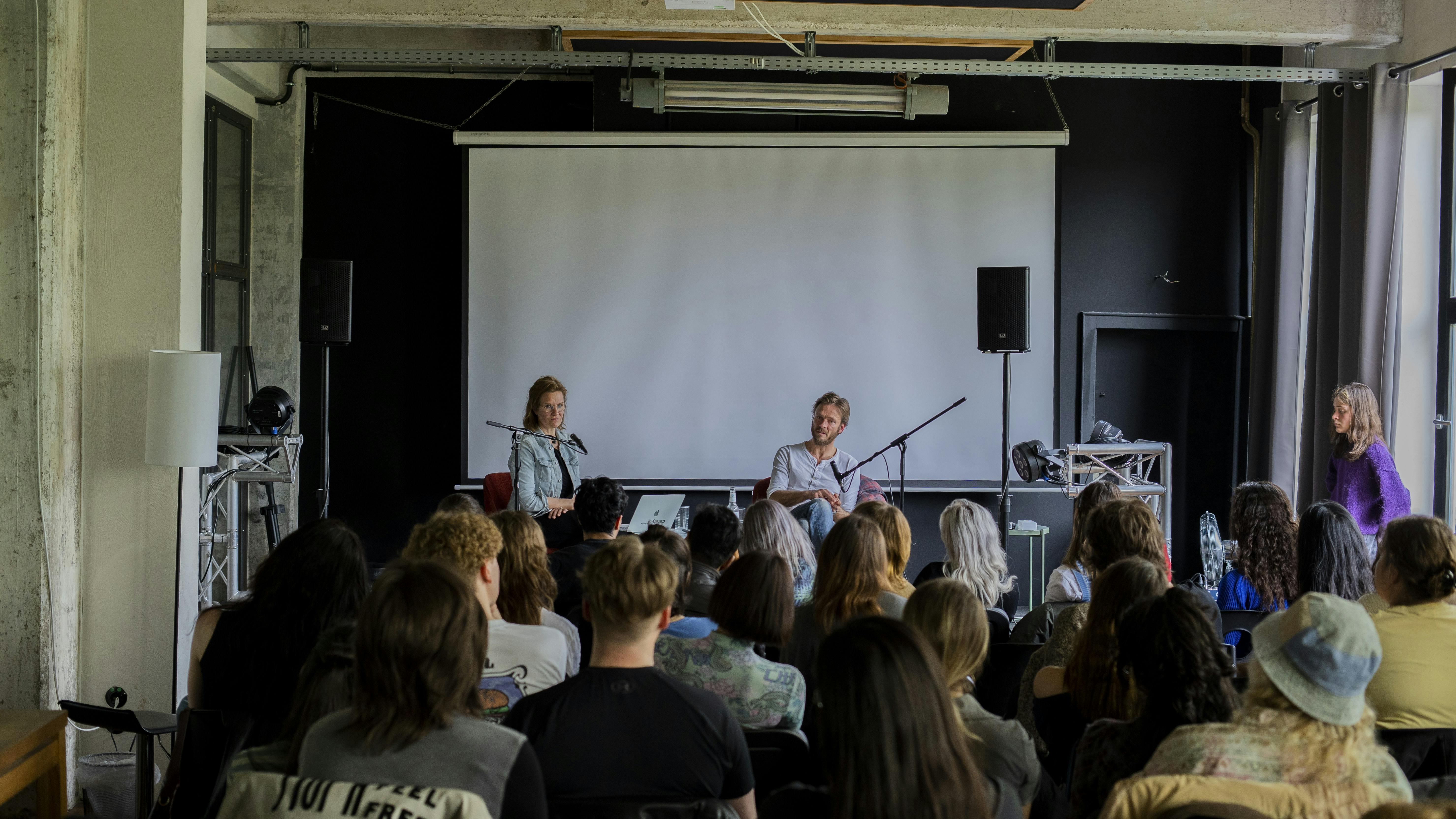 Andreas Pietschmann and Sylvia Schwarz in discuss on stage, in front of an audience of students