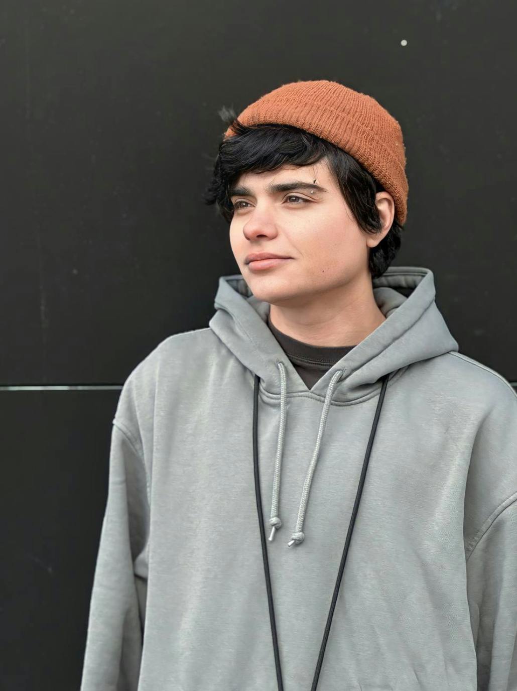 Quality Assurance Administrator Kris in a grey hoodie looks out calmly and confidently.