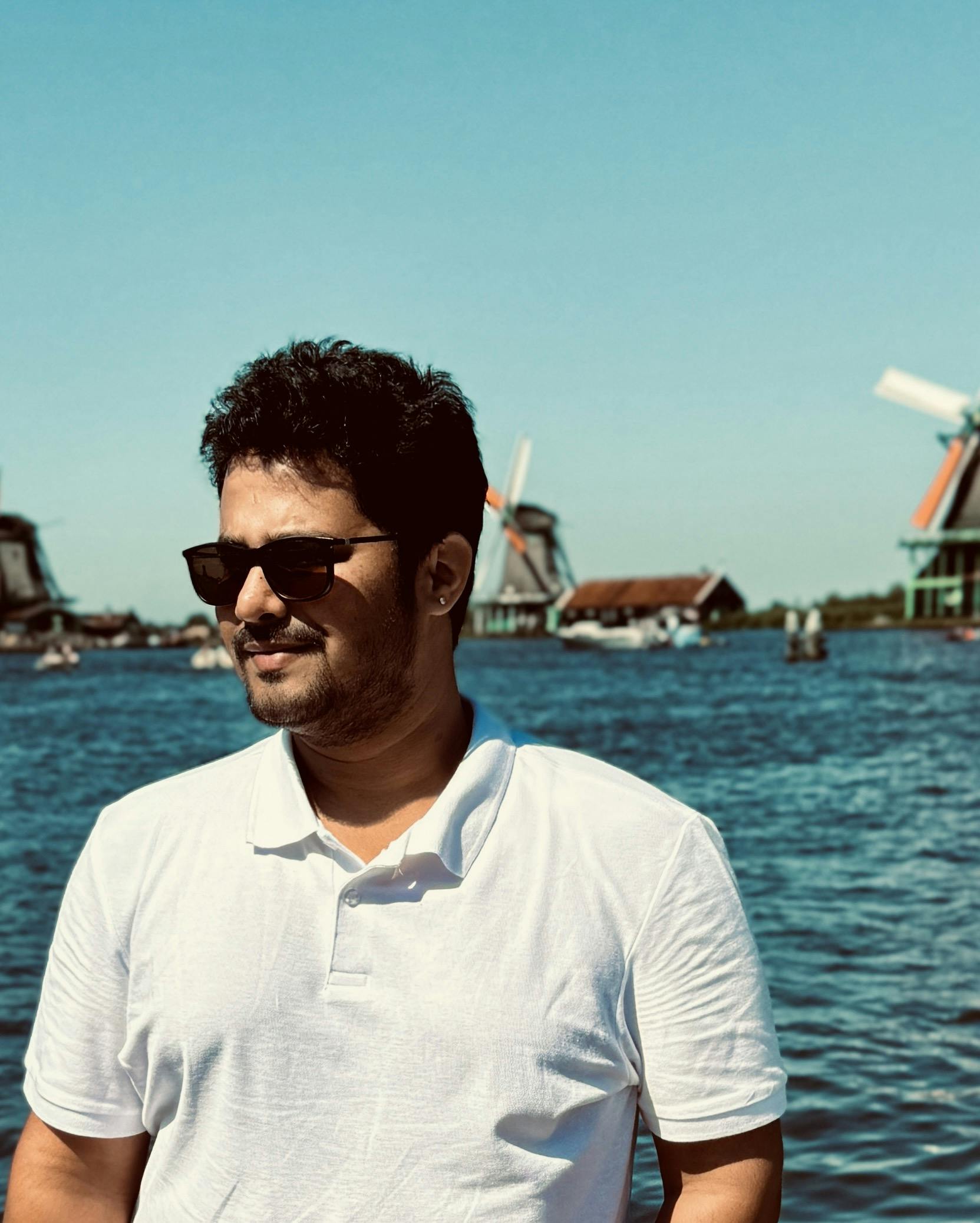 Mradul Kadam wearing sunglasses, exuding confidence and style, stands infront of a body of water.