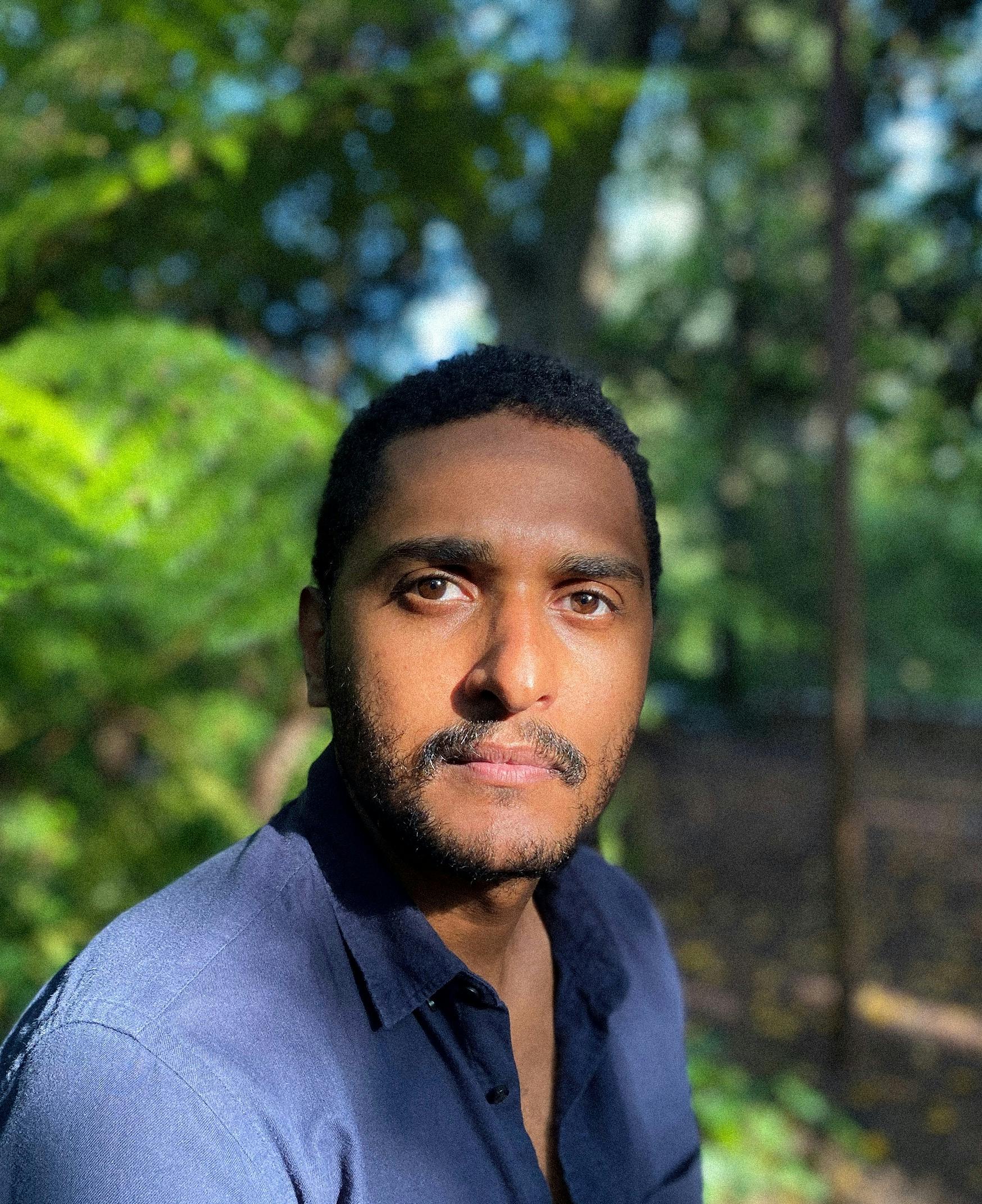 VFX tutor Carlos looks into the camera. He is in sunlight, leafy nature behind him