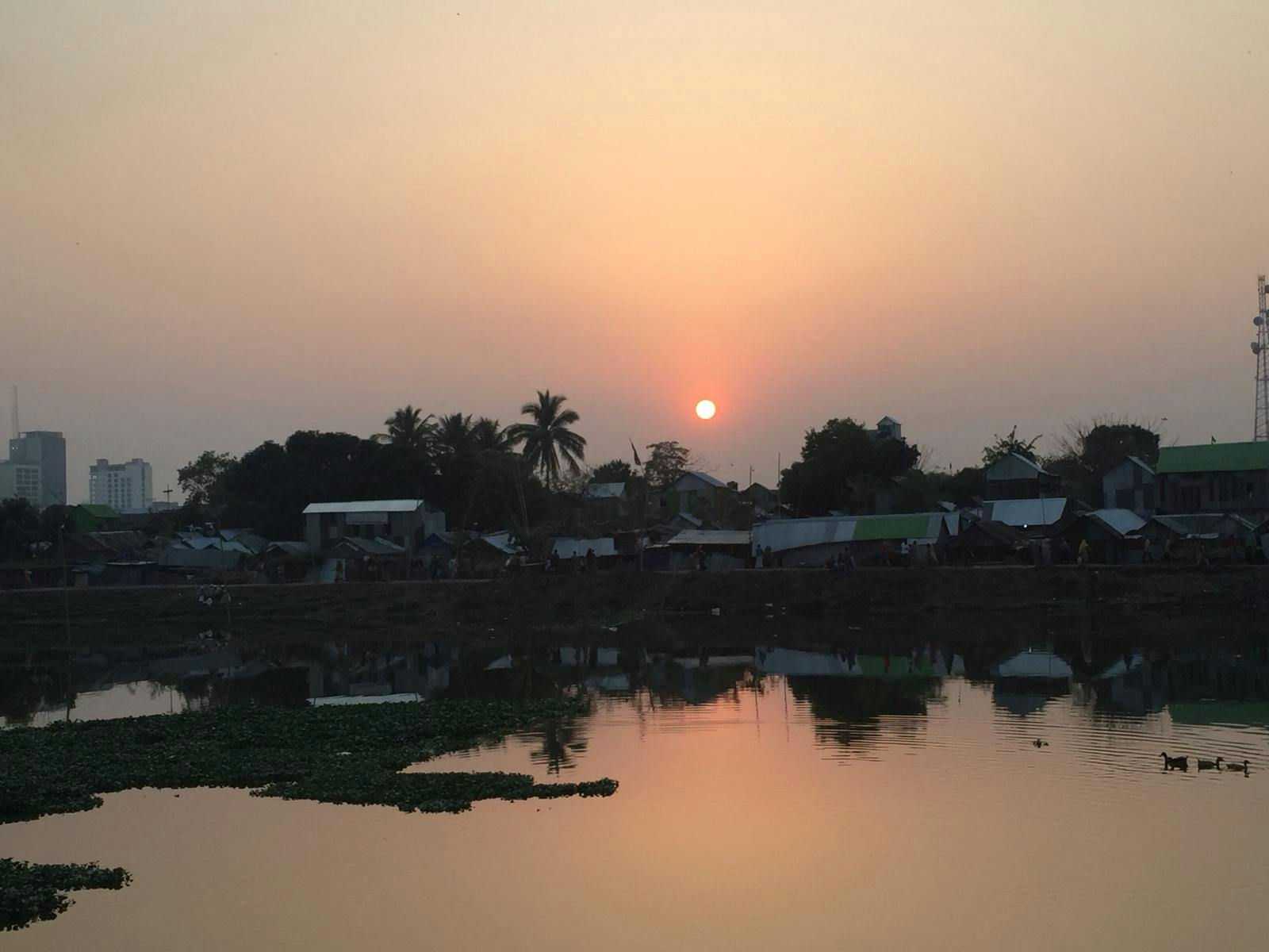 Still from Wherever I Am, the Sky Is Mine. The sun is setting over a built up area of land on the Indian subcontinent