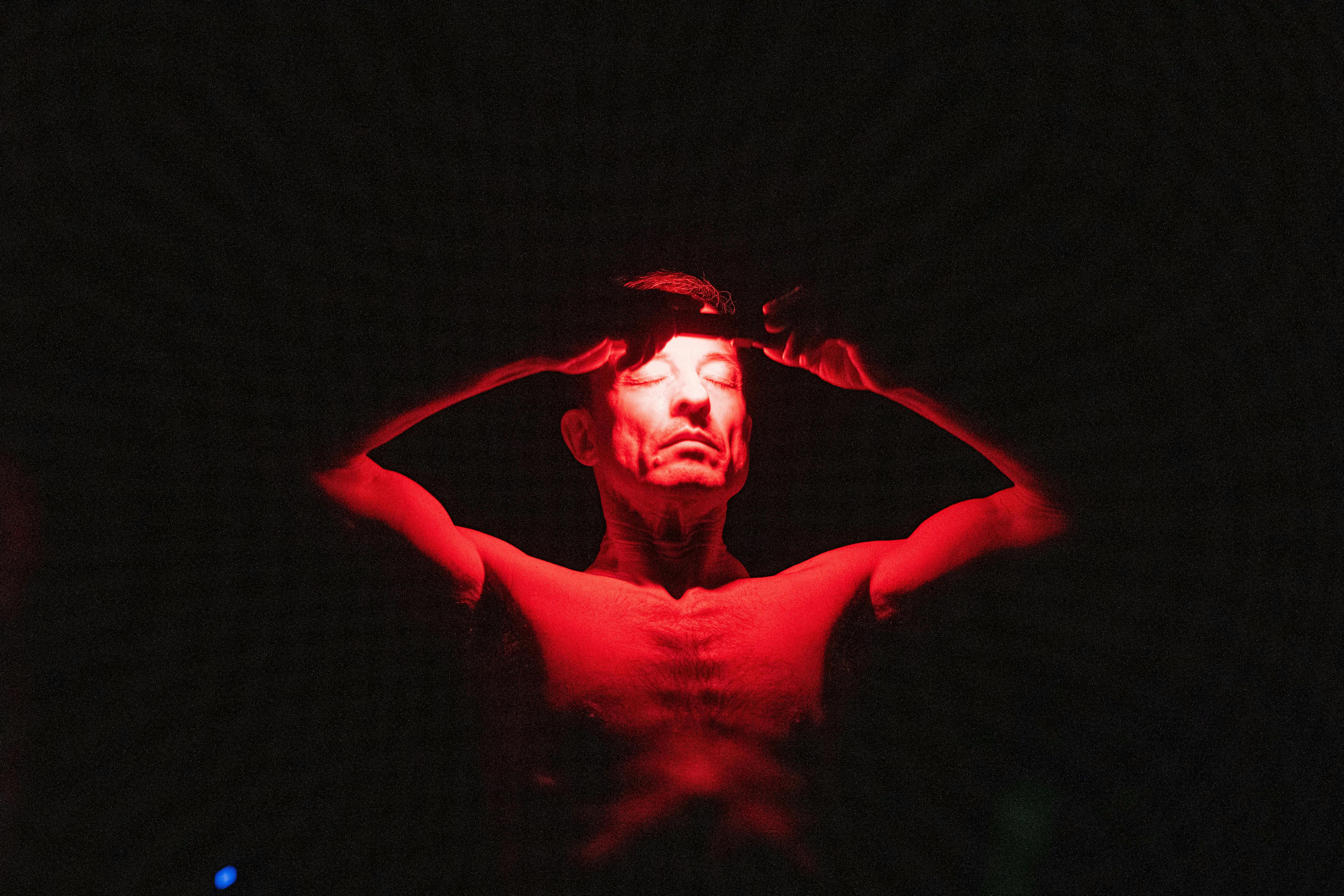 Dancer onstage holds a dramatic red light to his forehead