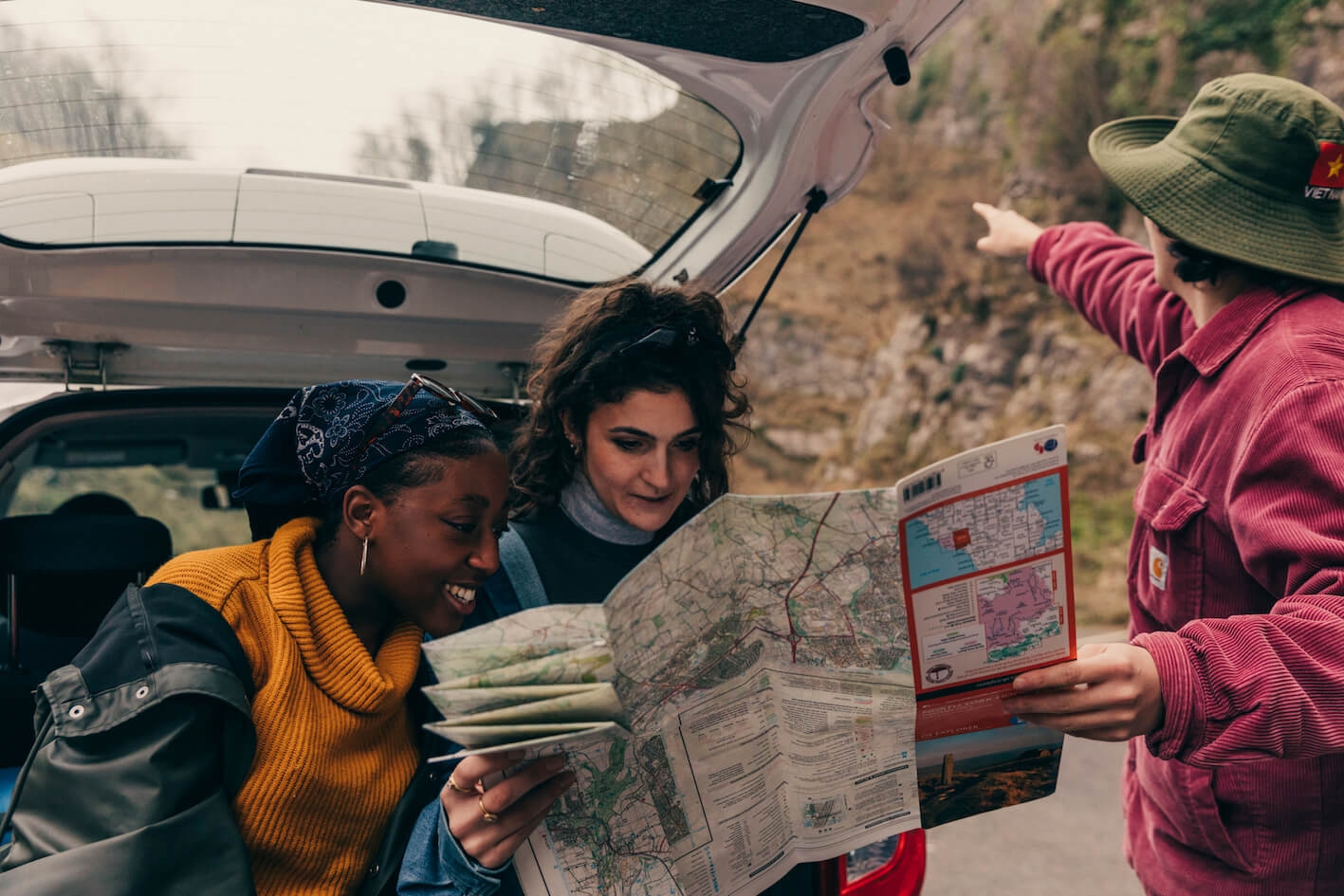 Three young adults looking at a map whilst gathering round the back of a car