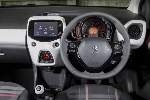The interior of a Puegeot 108 with steering wheel and dashboard in shot