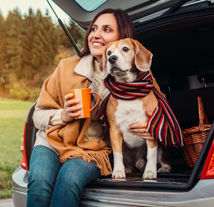 Lady sipping a hot drink with her dog in the back of a car